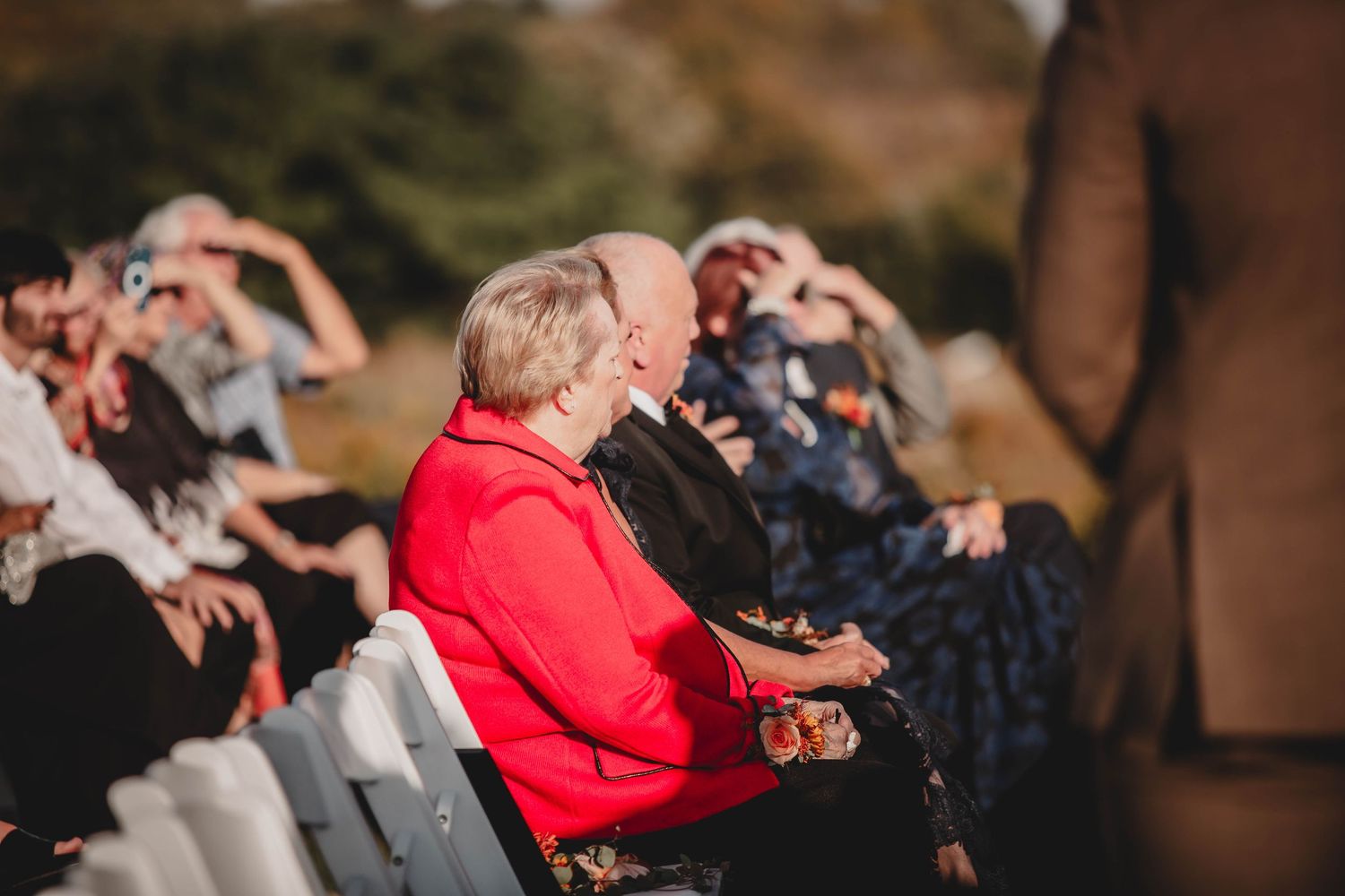 Wedding guests seated in white chairs during an outdoor ceremony.