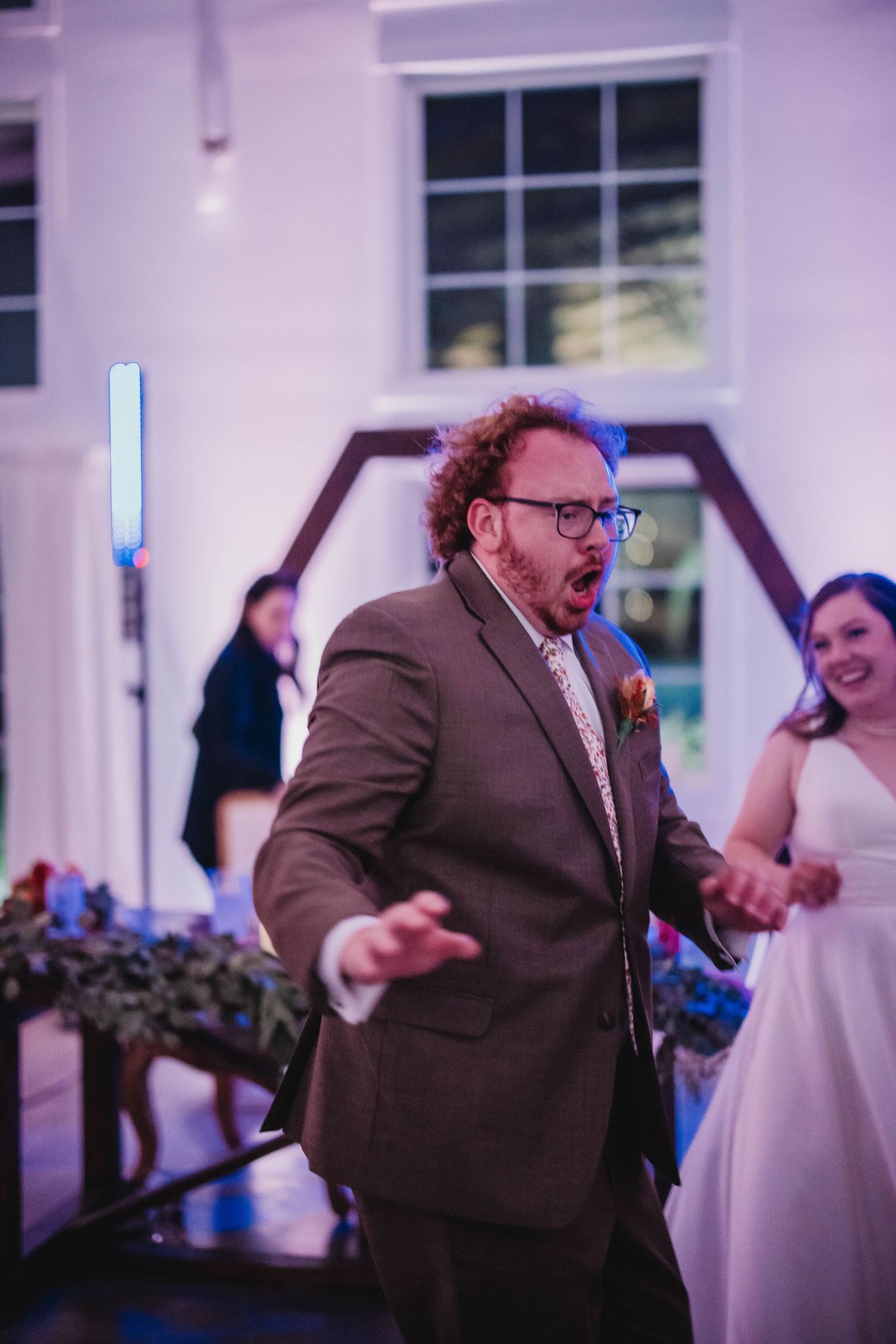 A wedding guest in a brown suit dances energetically at the reception.