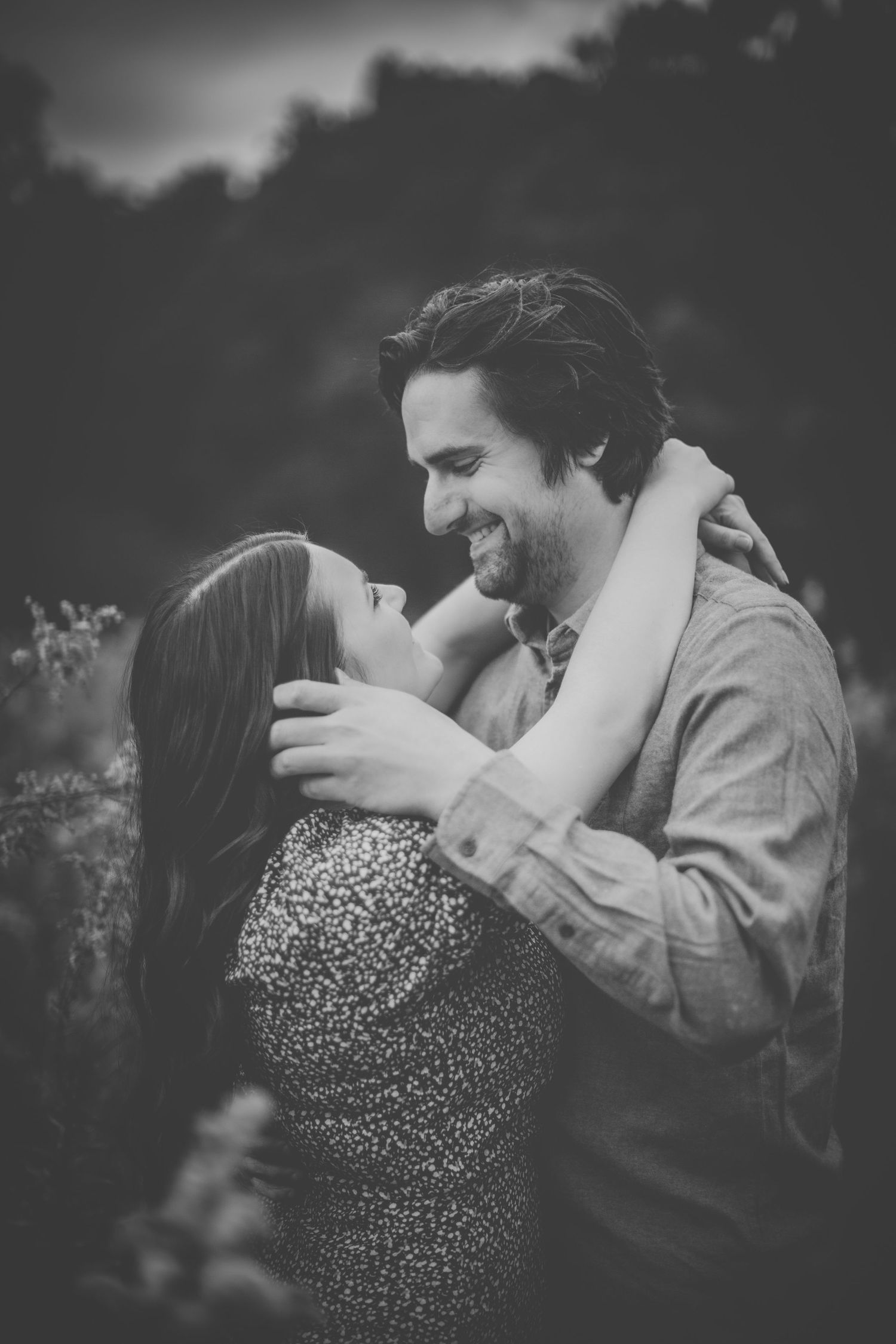 Black and white photo of a couple embracing in a natural outdoor setting.