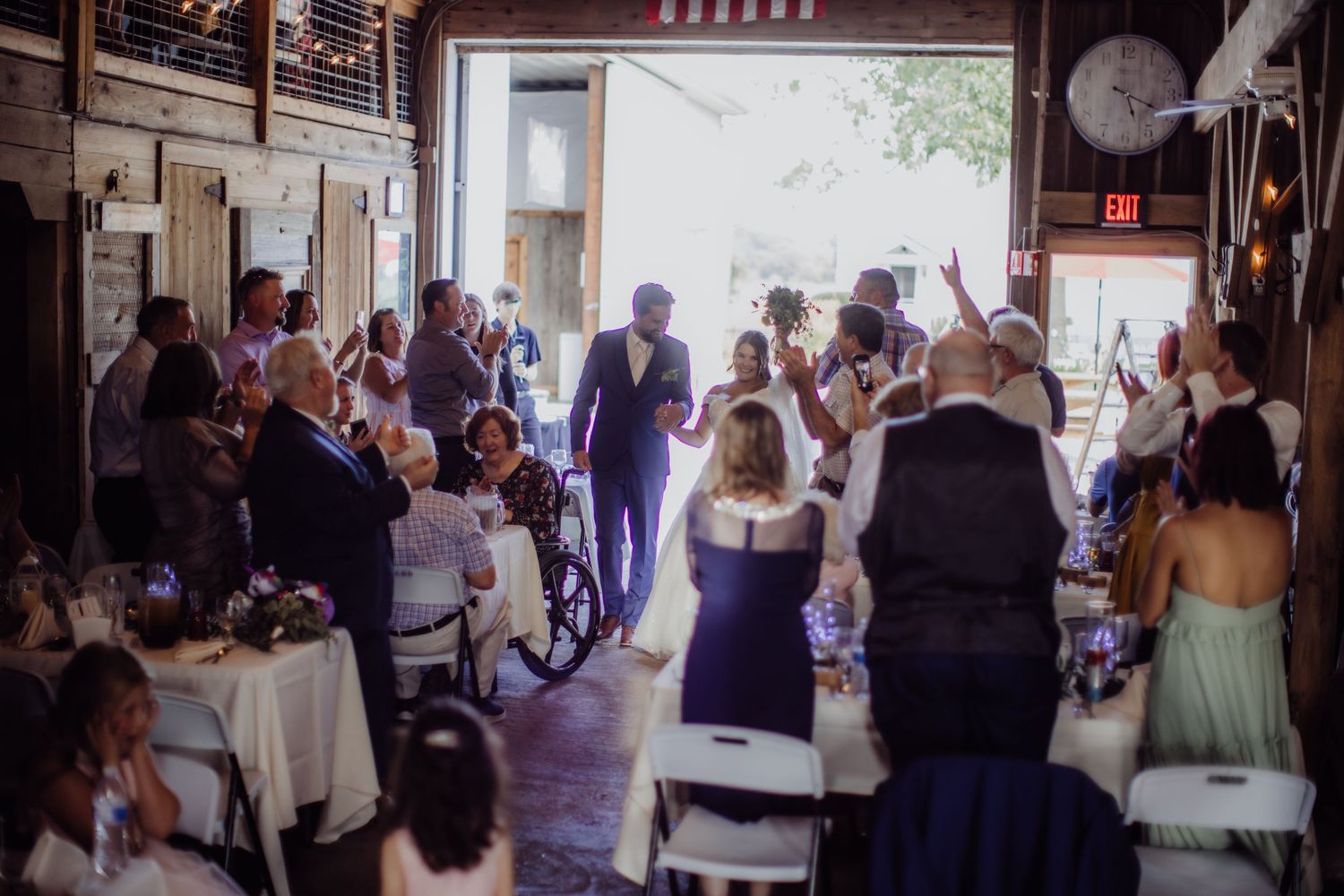 Wedding reception guests celebrate inside a rustic barn venue with American flag decor.
