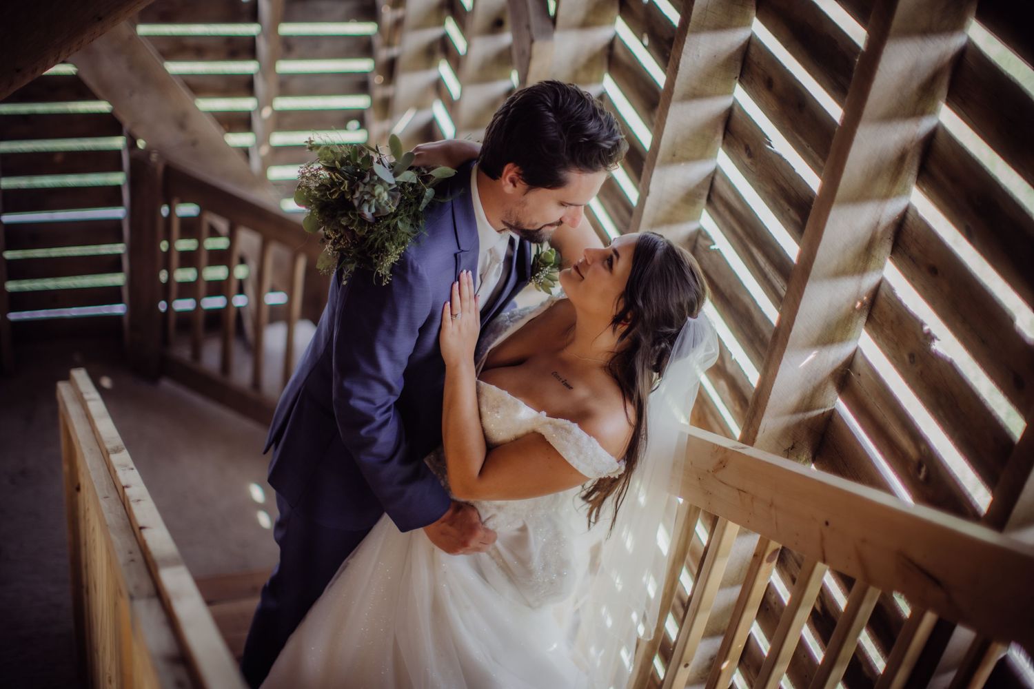 Romantic wedding portrait of couple embracing on wooden stairs with dramatic lighting.