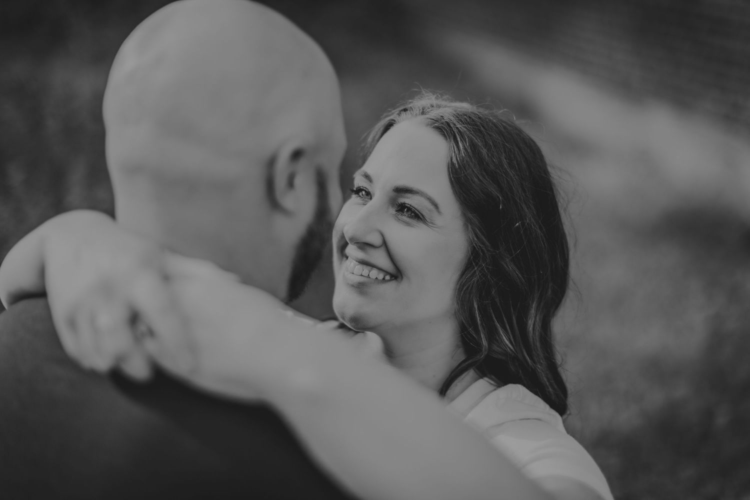 A romantic black and white portrait of a couple embracing and smiling during an outdoor photoshoot.