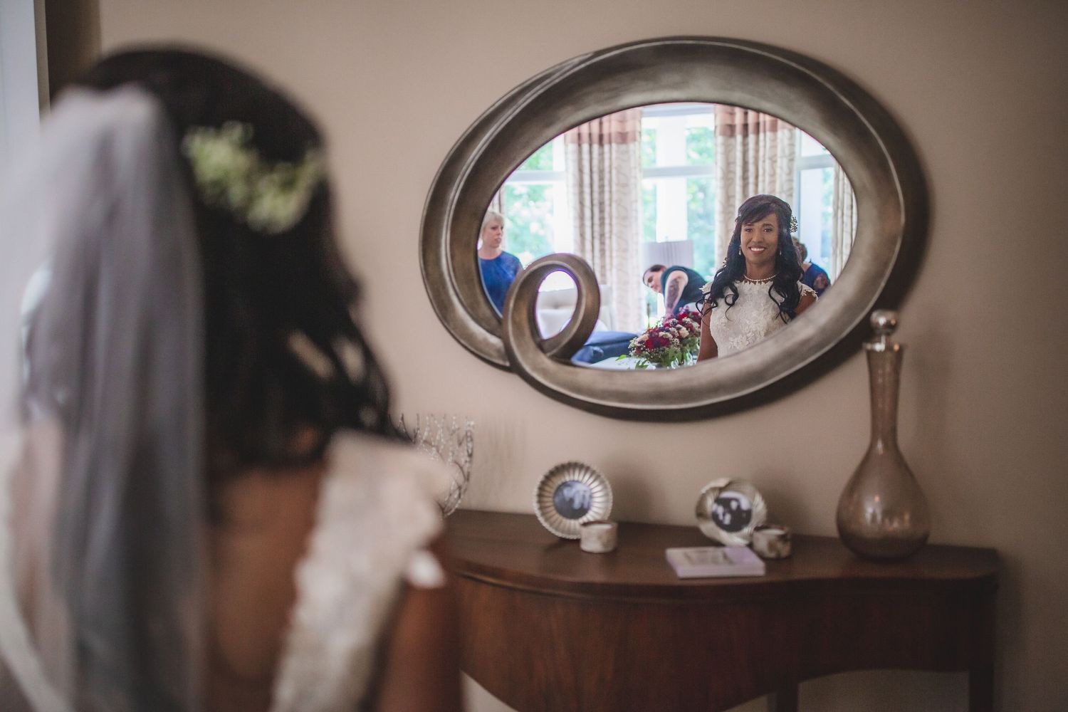 A bride admires her reflection in an oval mirror while getting ready on her wedding day.