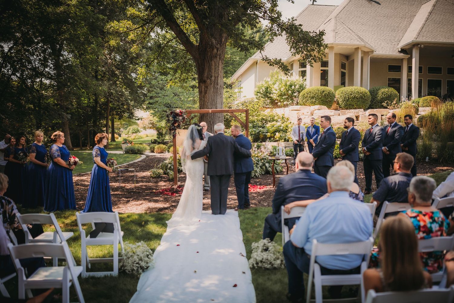 Panoramic view of an elegant outdoor wedding ceremony setup with white chairs and natural landscaping.
