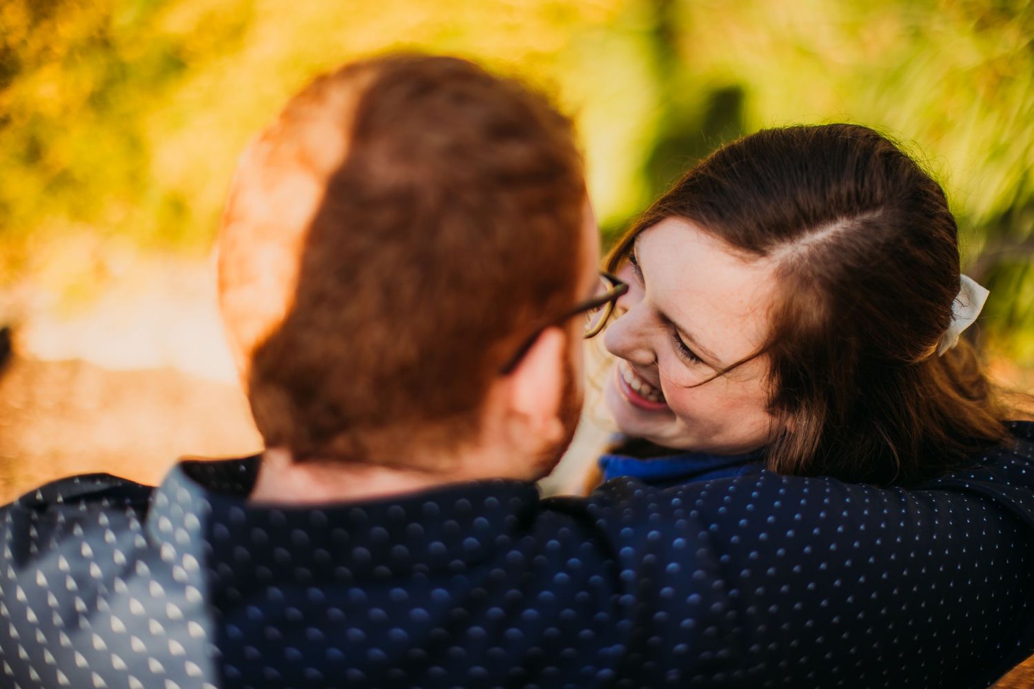 An intimate portrait captures a couple's affectionate moment against a sunlit natural background.