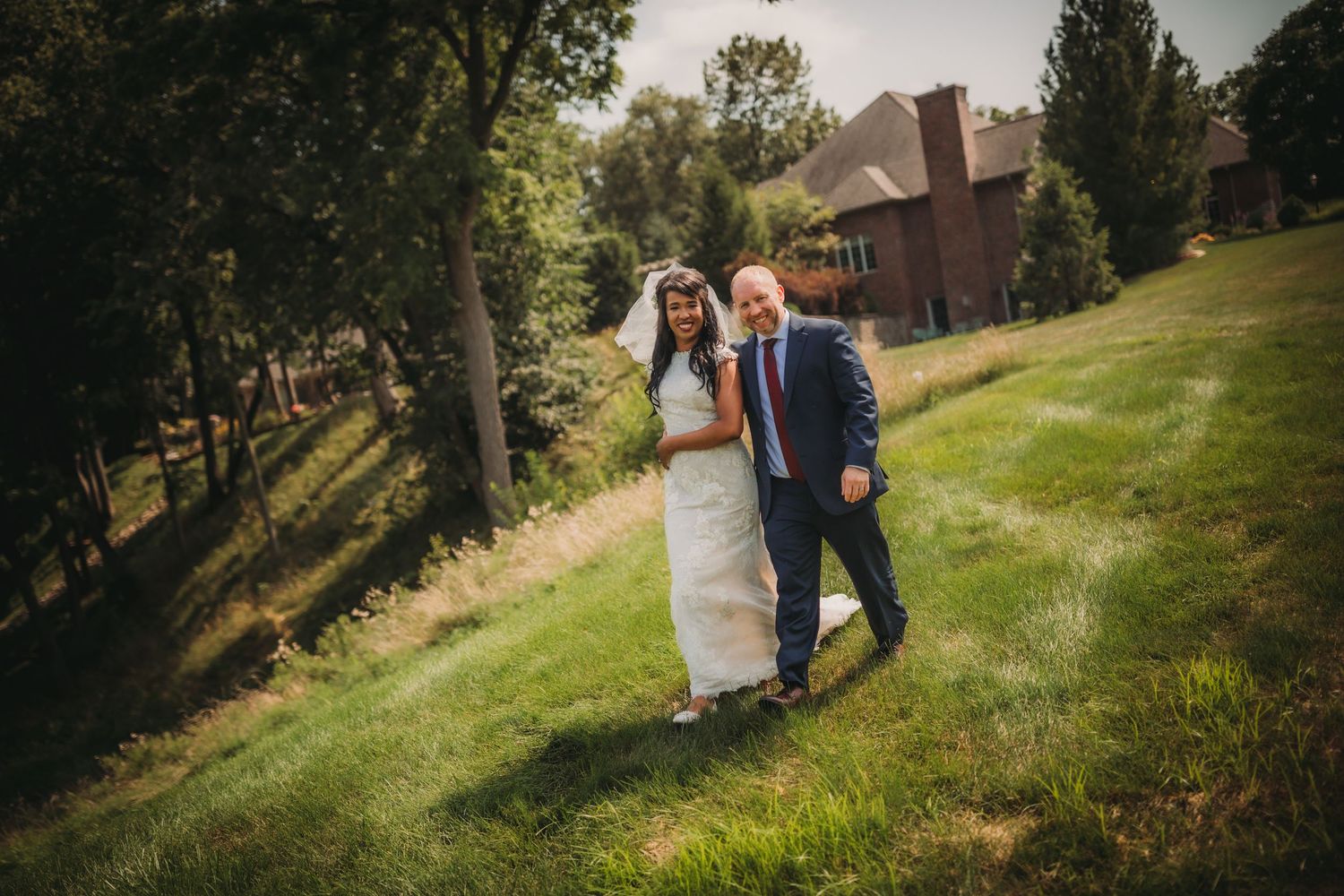 A couple walks together on a grassy hillside with brick buildings in the background.