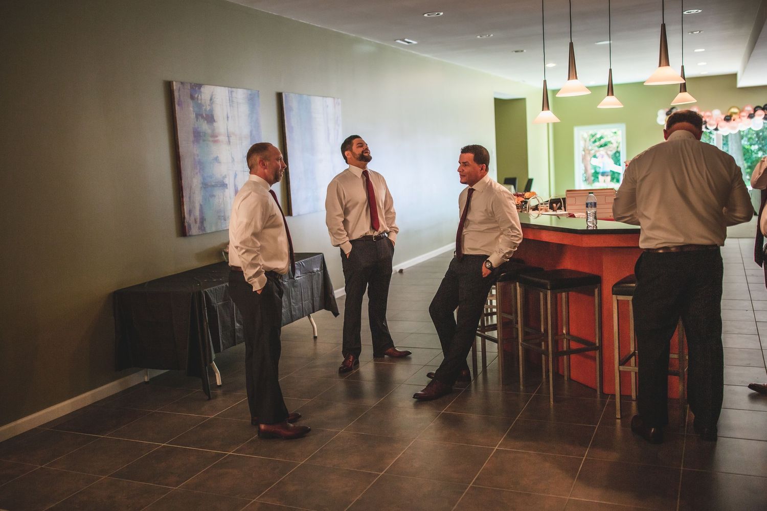 Group of people in formal attire gathered around kitchen bar area.