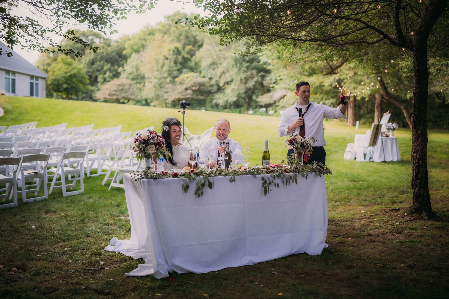 Long banquet tables with white linens and floral decor arranged for an outdoor wedding reception.
