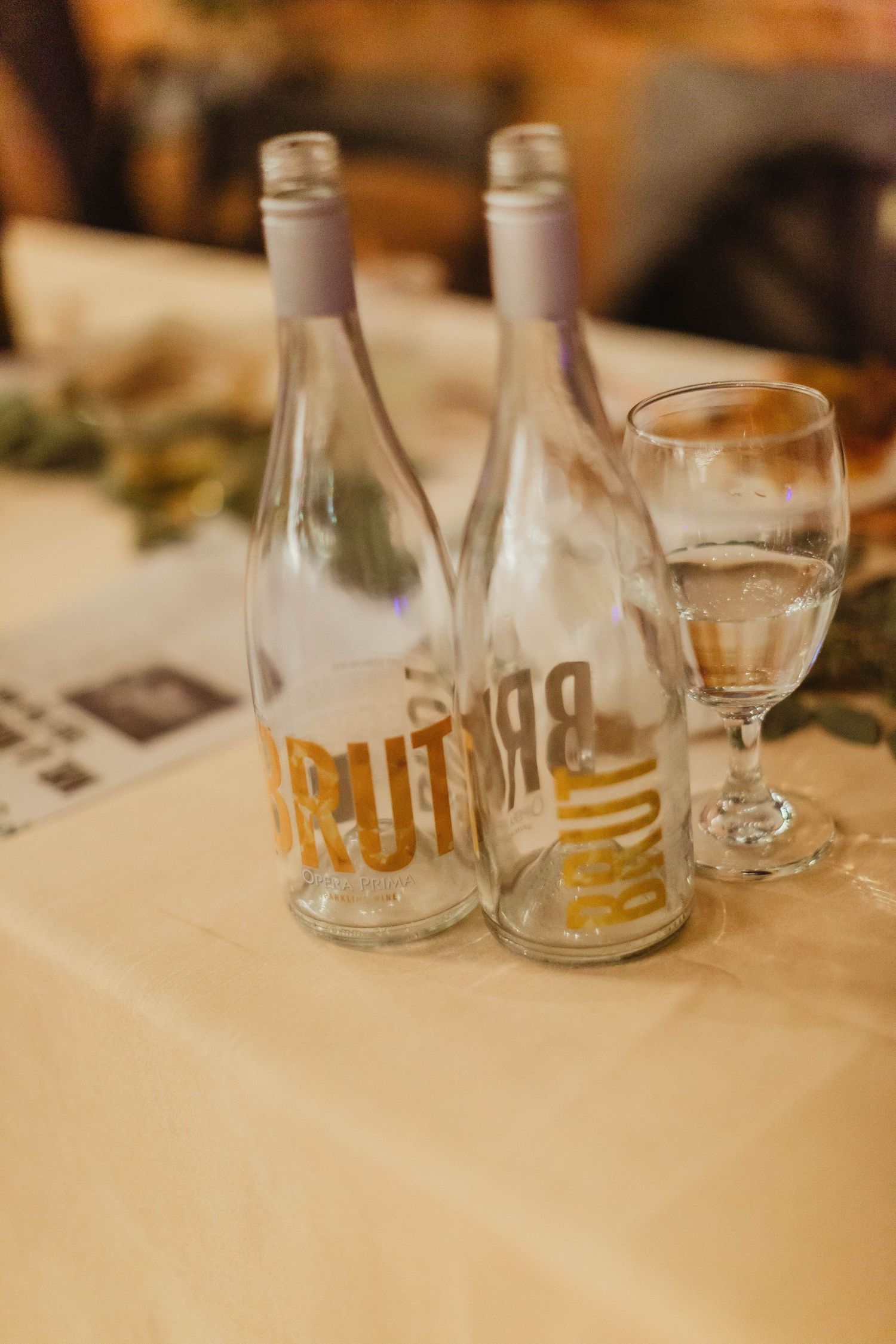Two clear glass bottles and wine glass on white tablecloth.