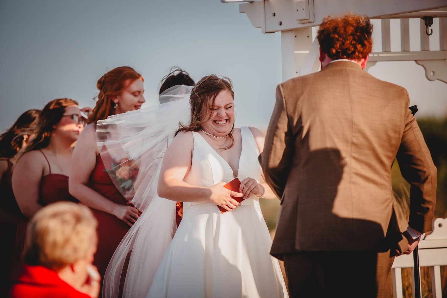 Wedding ceremony participants share joyful moment under white pergola.