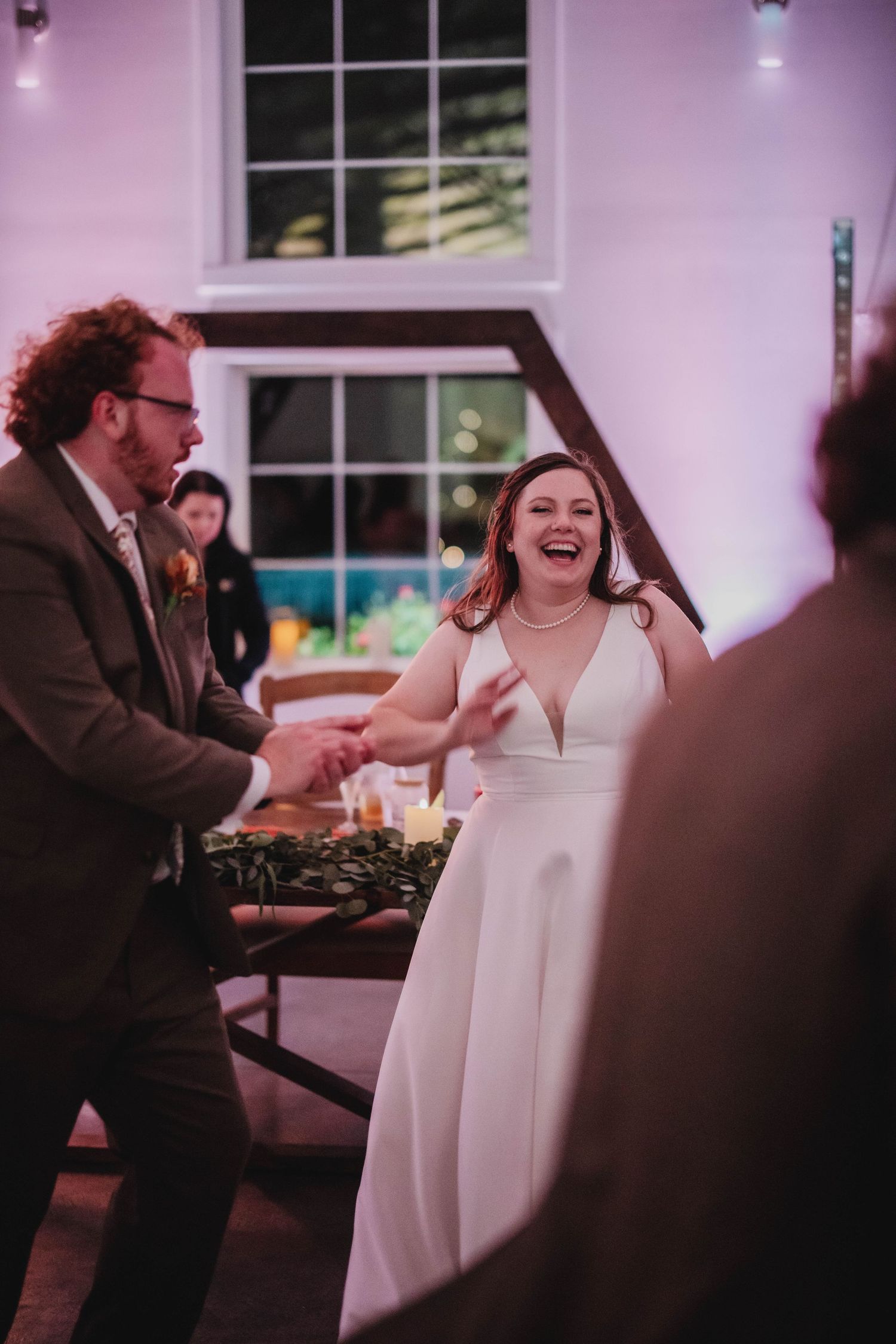 Guests share an animated moment dancing at a wedding reception with pink lighting.