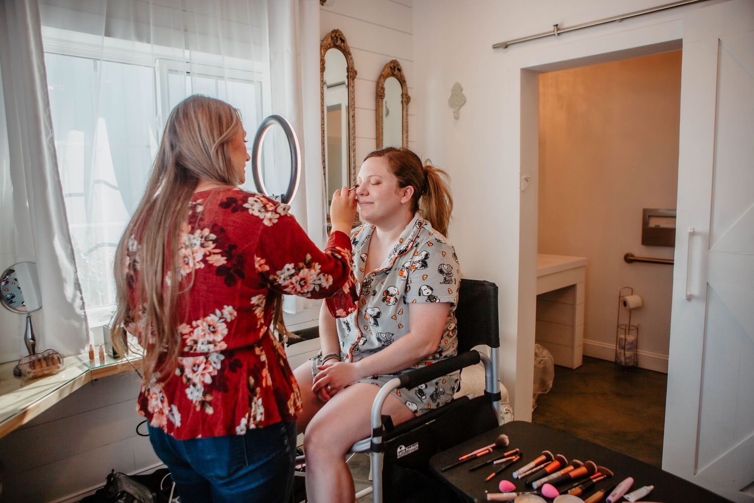 Makeup artist applying final touches in a bright, window-lit room.