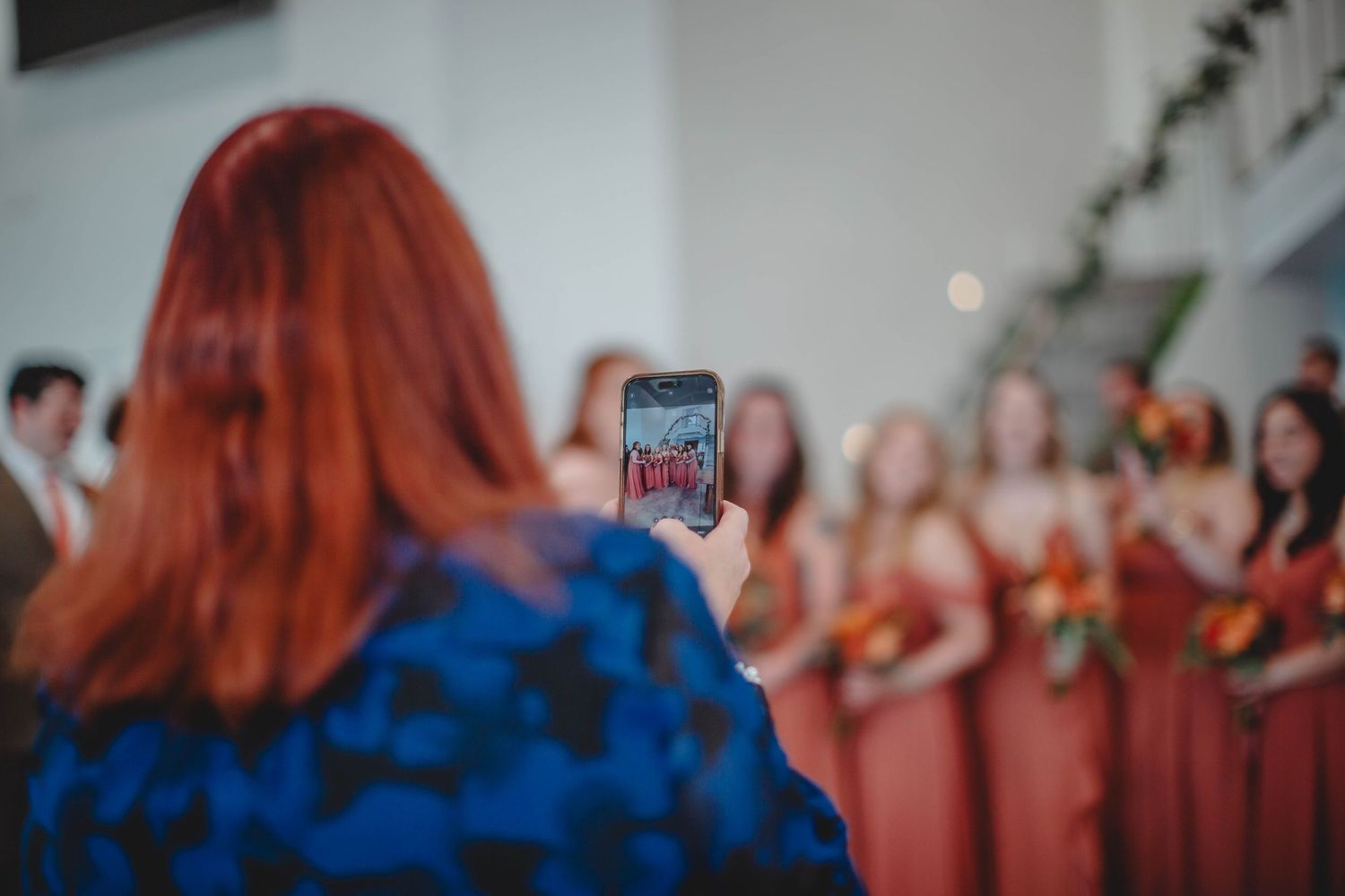 A person in blue taking a phone photo of bridesmaids in coral-colored dresses at a wedding.