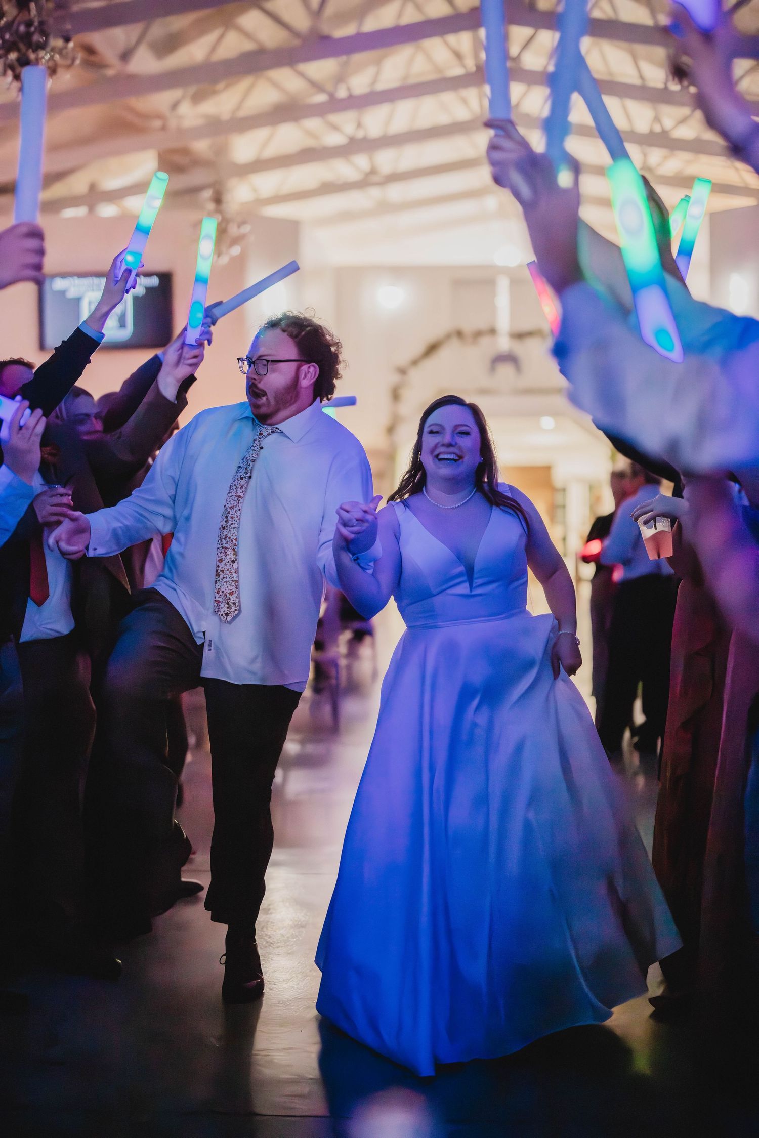 Couple celebrates on dance floor while wedding guests wave LED light sticks in festive atmosphere.