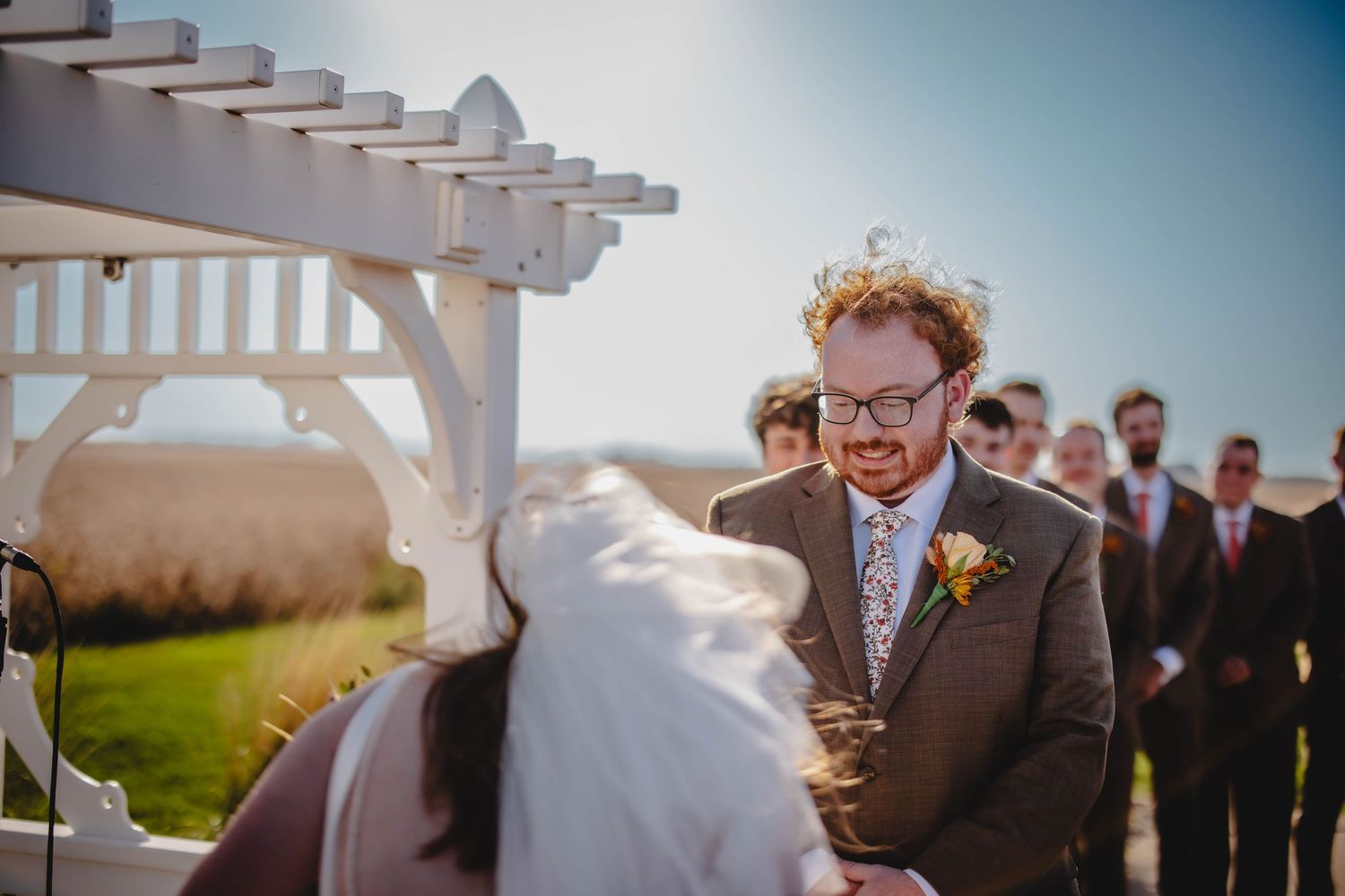 Couple exchanging vows under white pergola during outdoor countryside wedding.