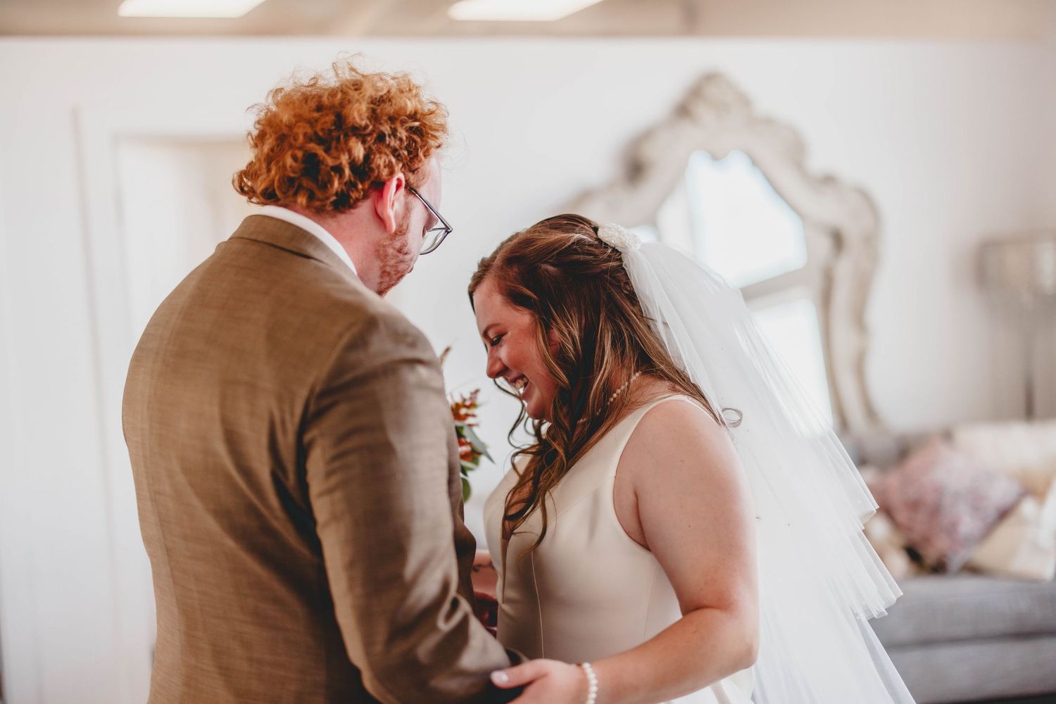 Tender moment between newlyweds during first look ceremony in elegant white room.