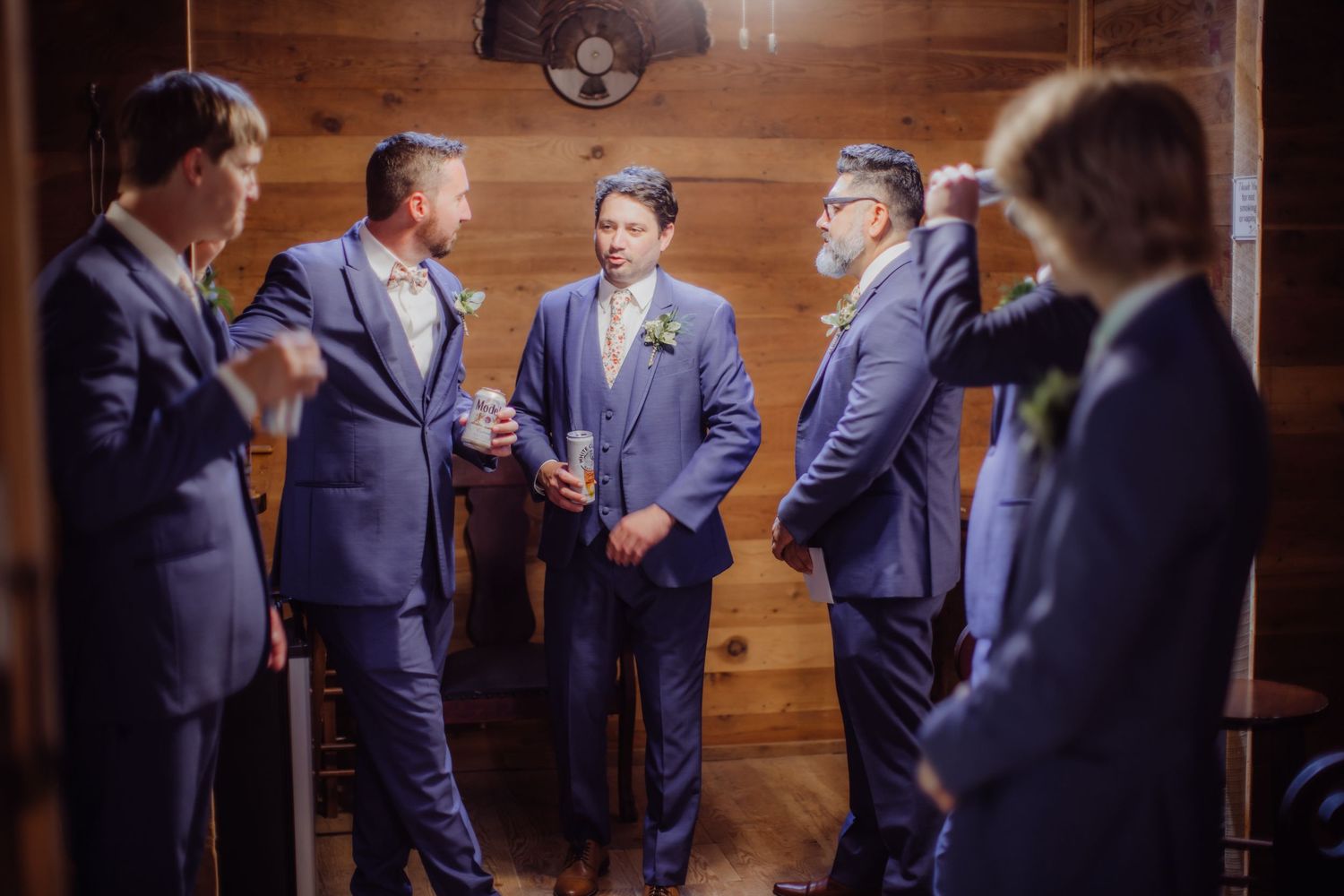 Groomsmen in navy suits having conversation in wood-paneled room.