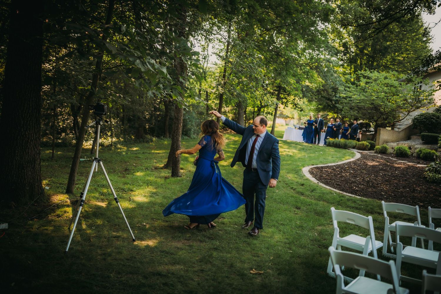 Couple in formal attire walks through garden wedding ceremony setup.