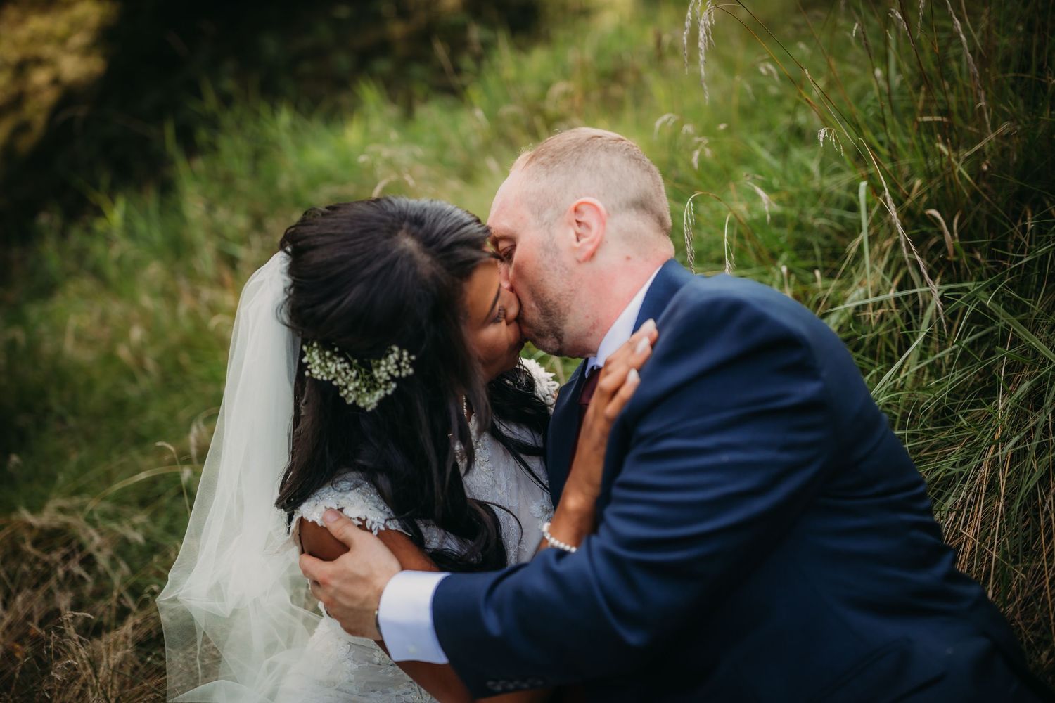 A romantic wedding couple shares an intimate moment together in a grassy outdoor setting.