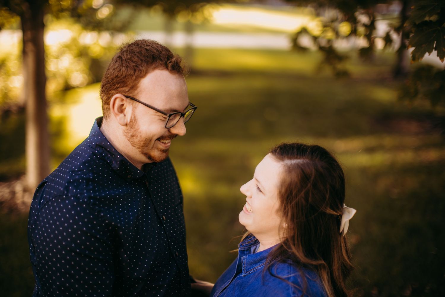 A couple sharing a lighthearted moment outdoors with natural sunlight filtering through trees.
