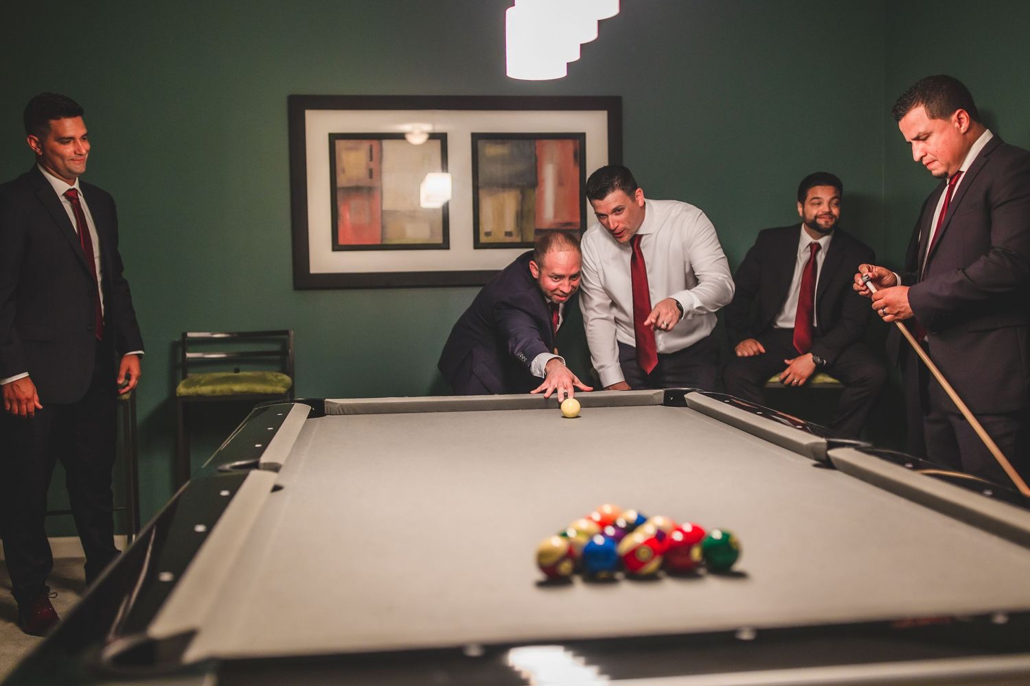 People in formal attire gathered around a pool table for a game break.