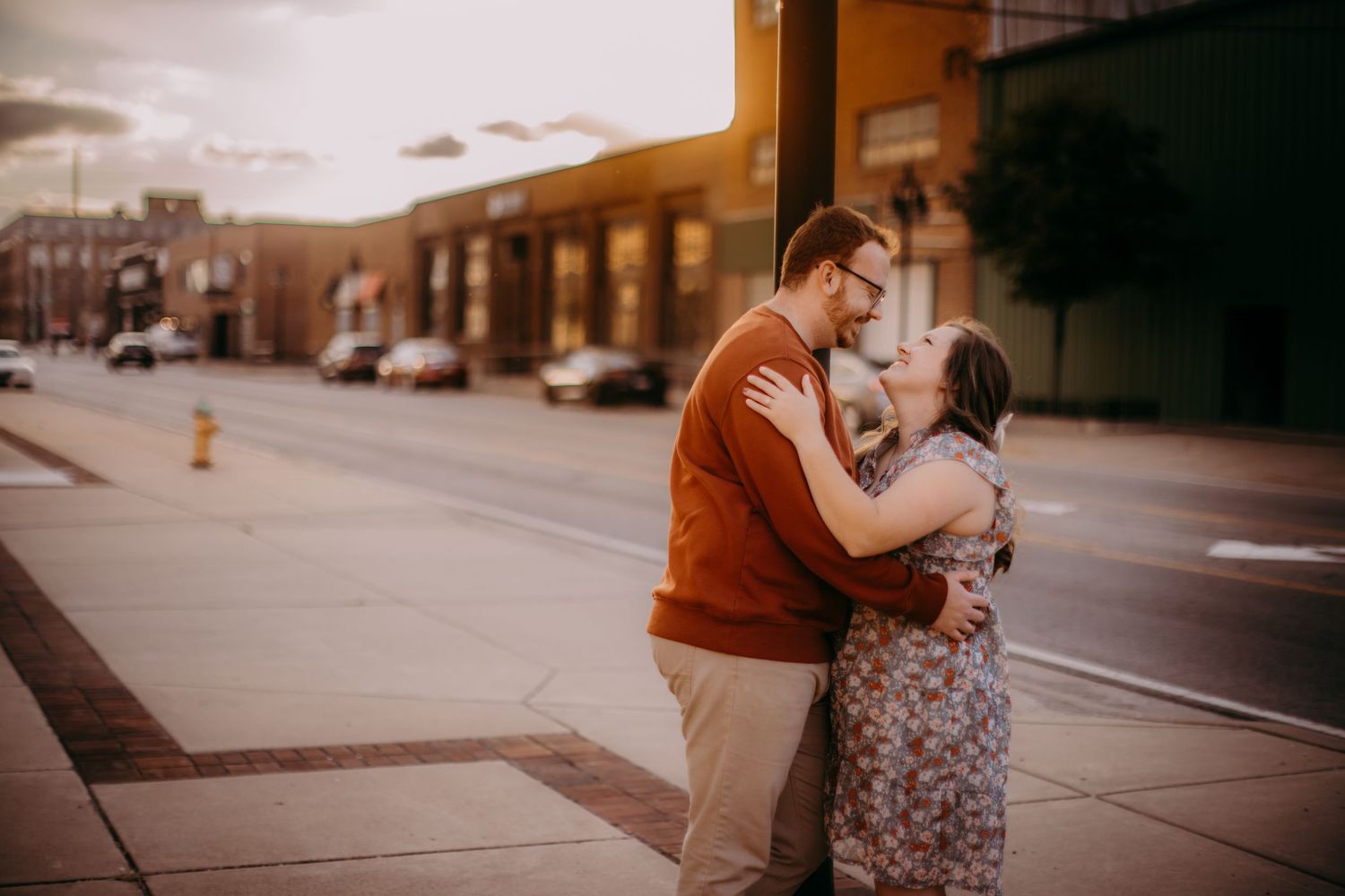 Urban engagement session shows a couple embracing on a quiet city sidewalk at sunset.