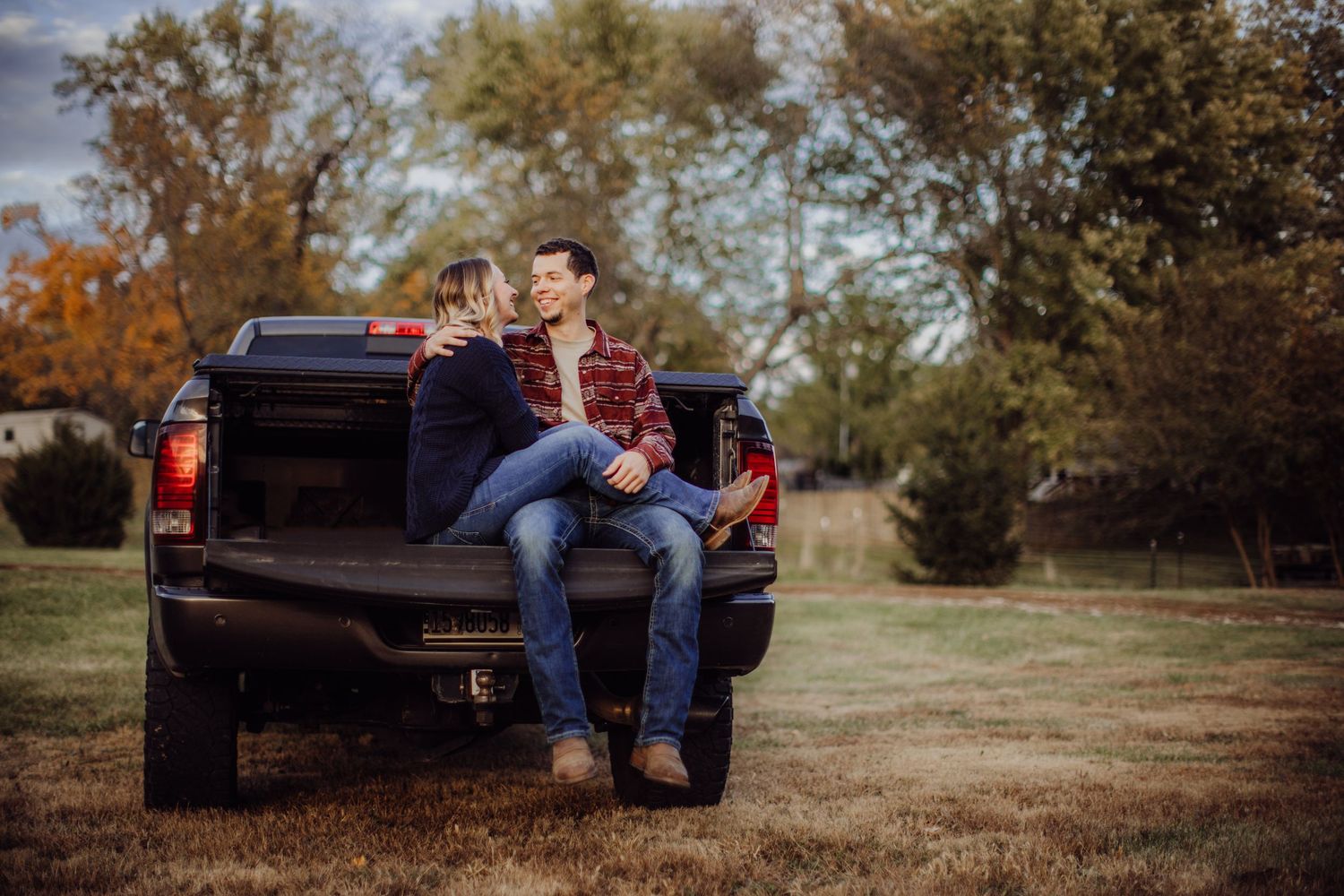 A couple enjoys a casual moment sitting together on their pickup truck in a fall setting.