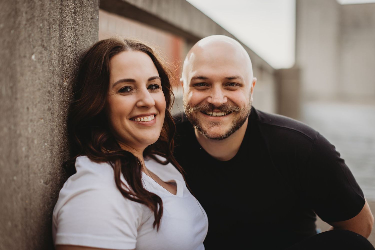 Candid moment of a couple laughing together against a concrete wall.