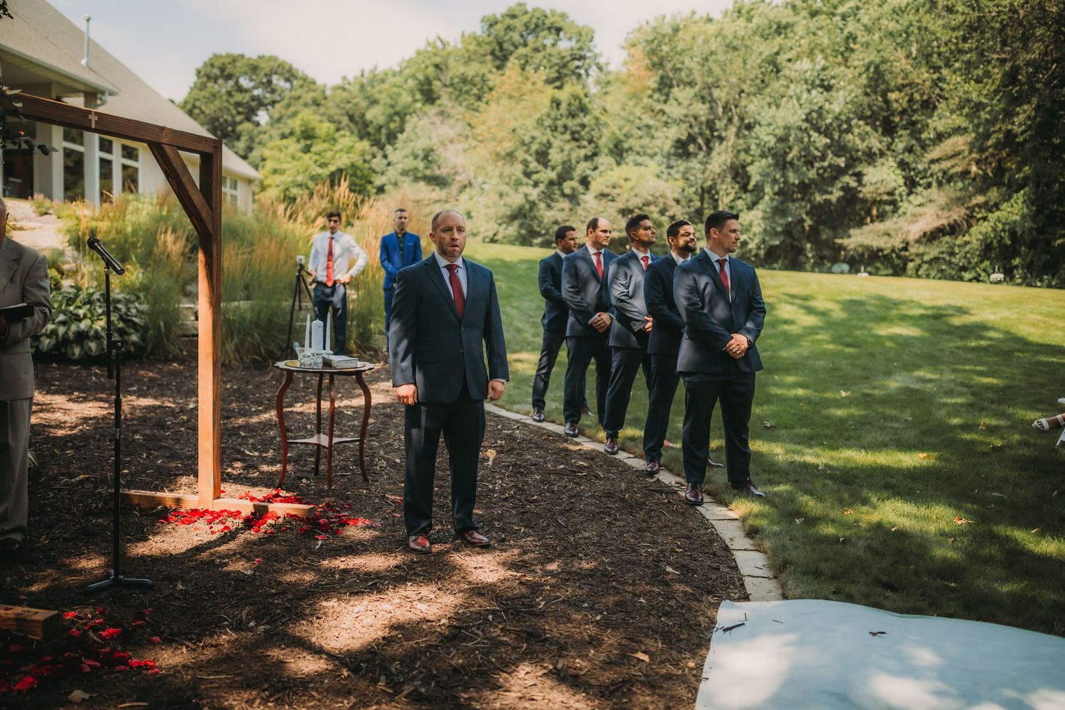 Groomsmen gather on a curved garden path before outdoor wedding ceremony.