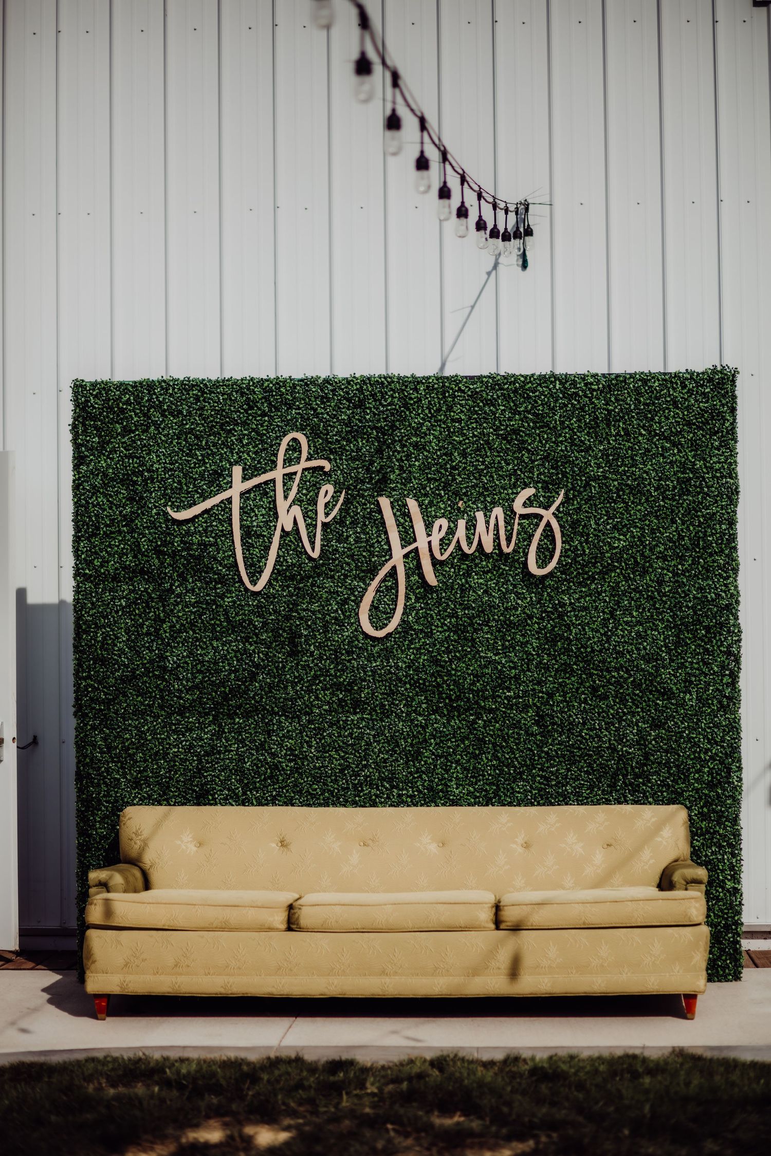 Modern event space featuring a cream-colored couch against a green hedge wall with script lettering.