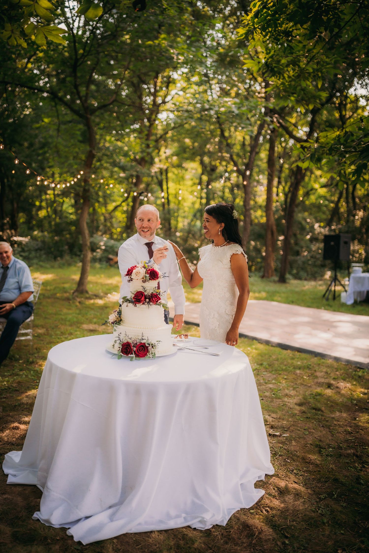 Wedding cake and document signing moment captured at an outdoor reception with natural forest backdrop.