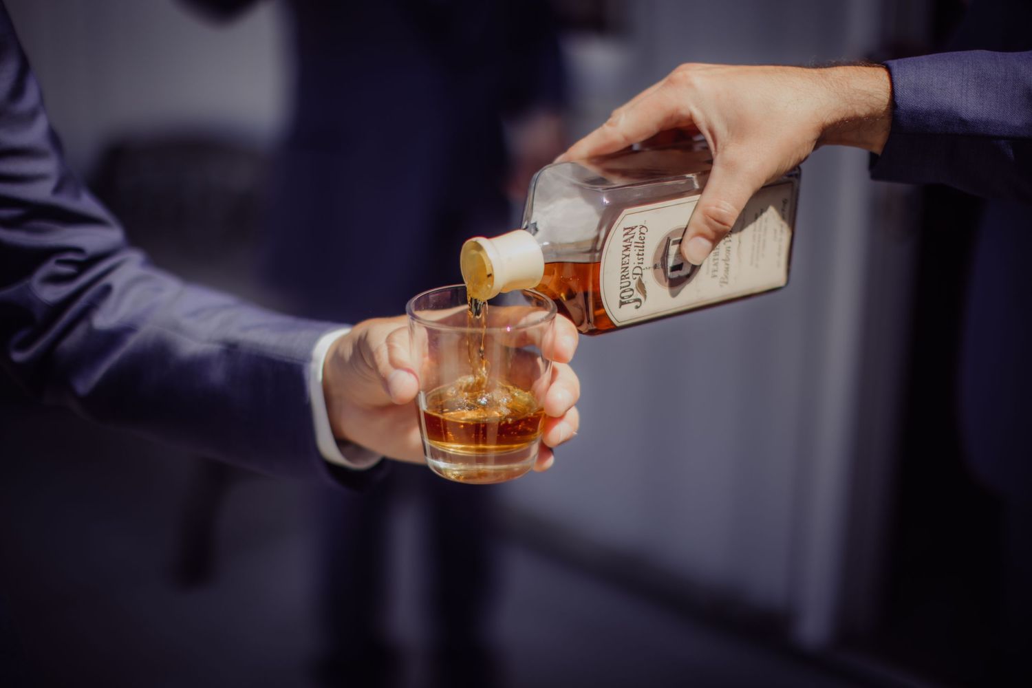 Hands pouring whiskey into a glass during wedding celebration.