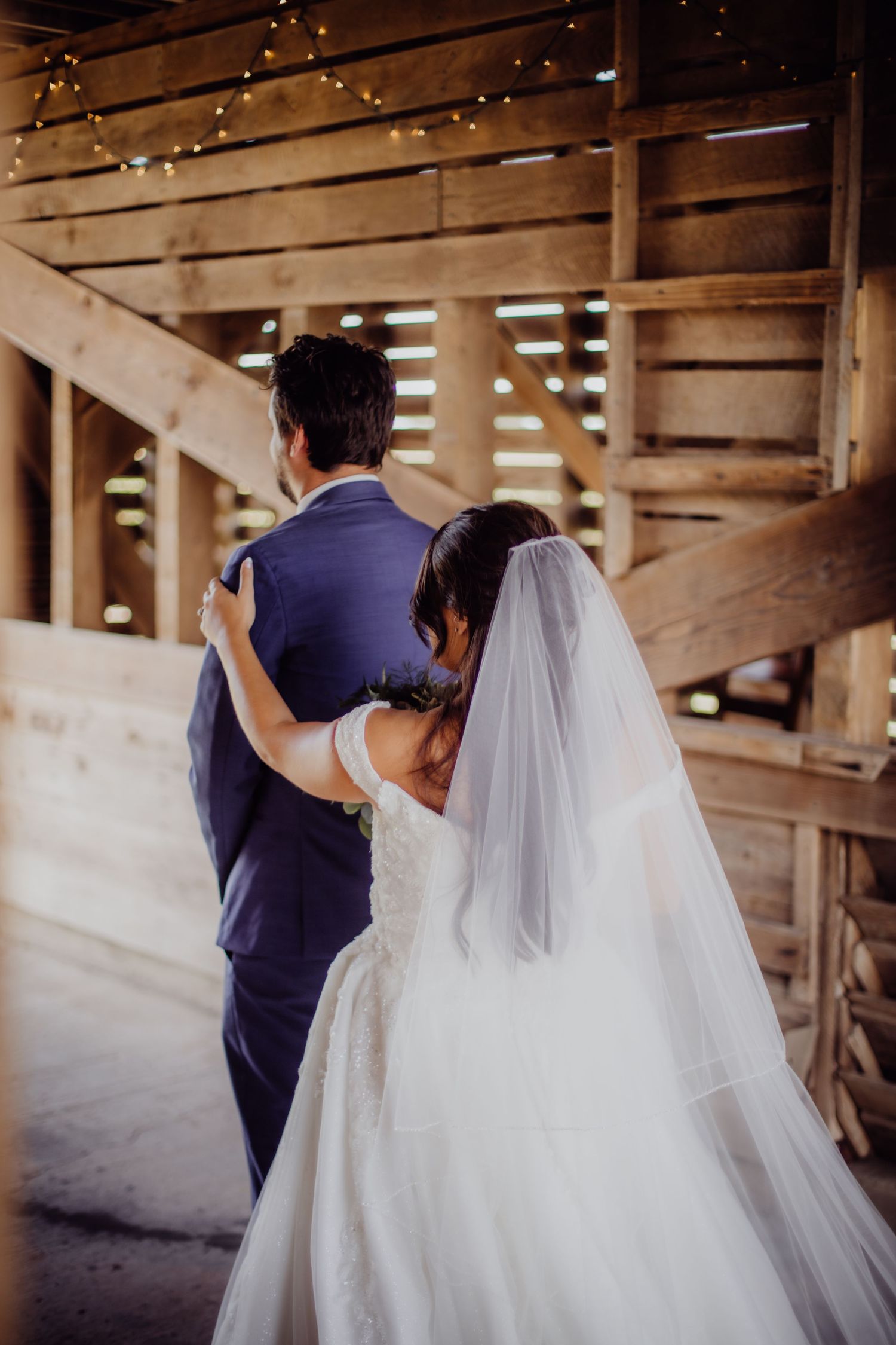 Emotional first look sequence between newlyweds in a sunlit rustic barn venue.