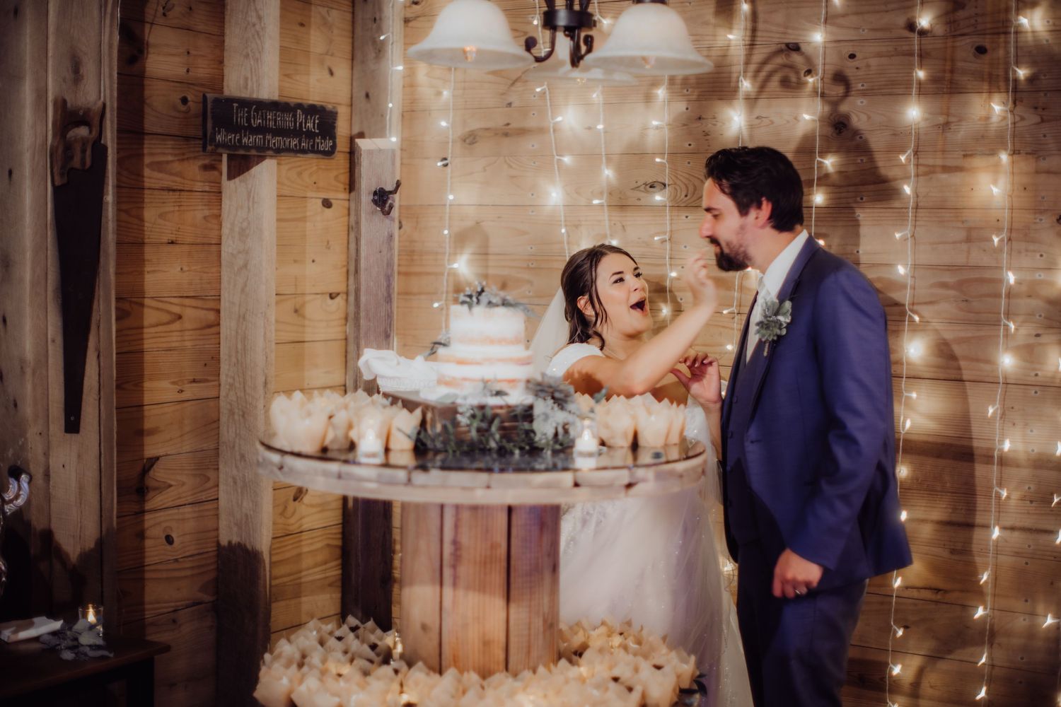 Newlyweds laugh together during their cake cutting ceremony at a rustic barn reception.