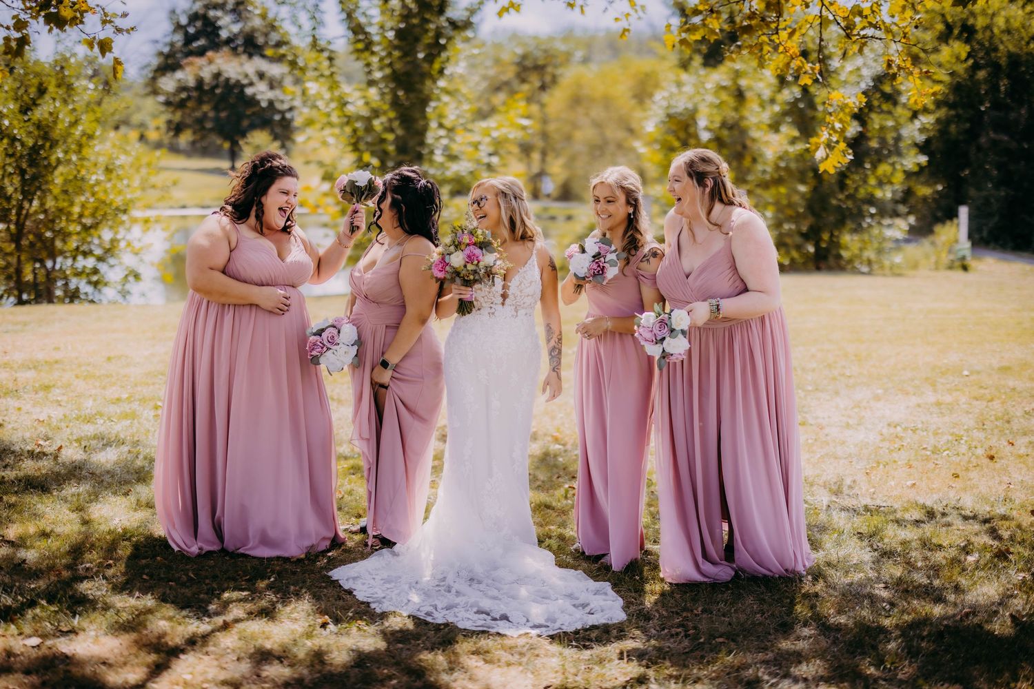 Bridesmaids in dusty rose dresses laugh together on a sunny autumn day.