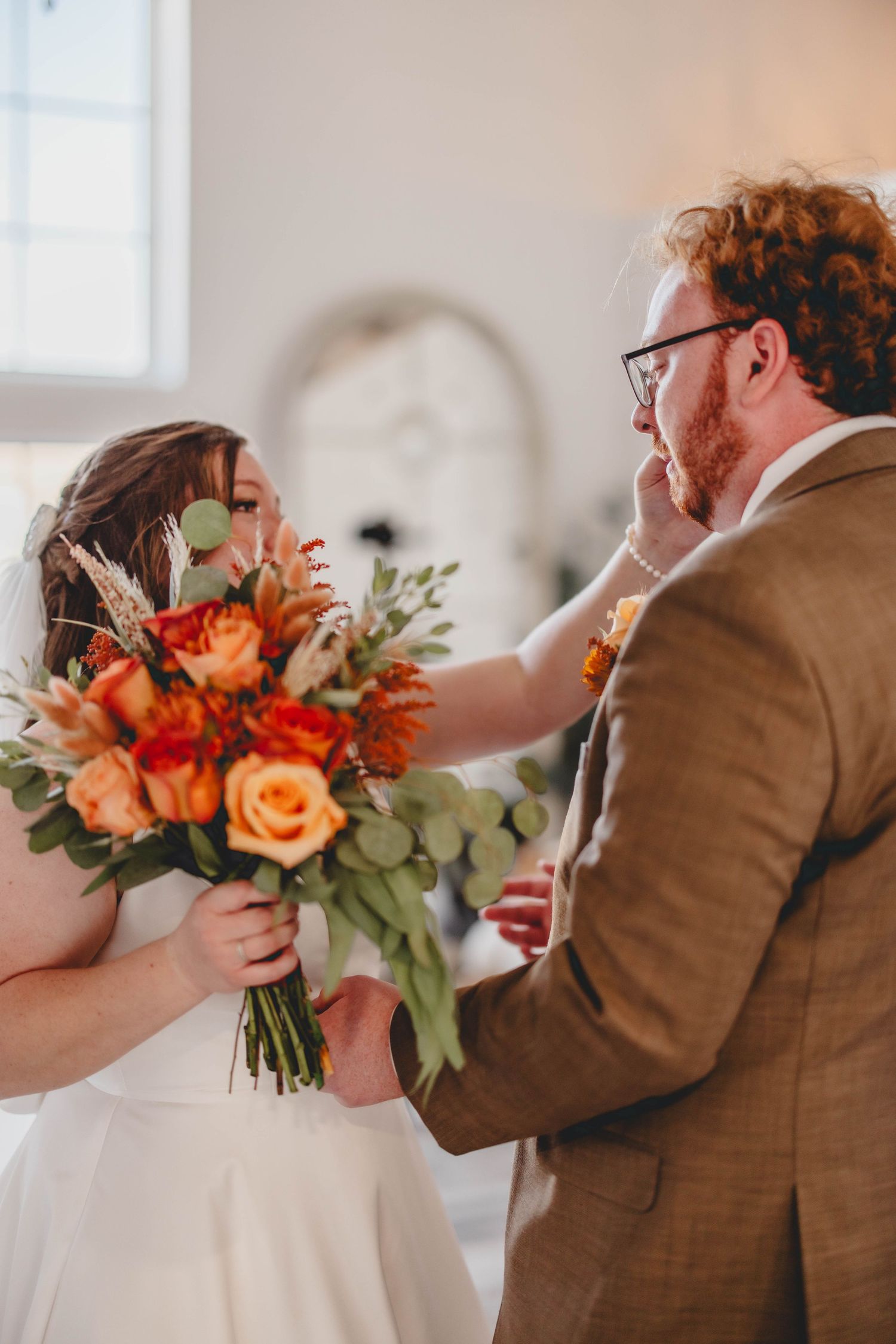 Intimate wedding moment captured as couple shares emotional first look with vibrant orange and coral bouquet.