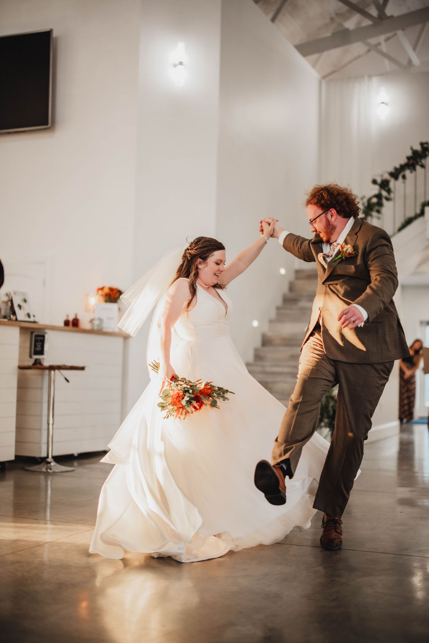 Newlyweds share a joyful dance moment with energetic movements in their modern reception space.