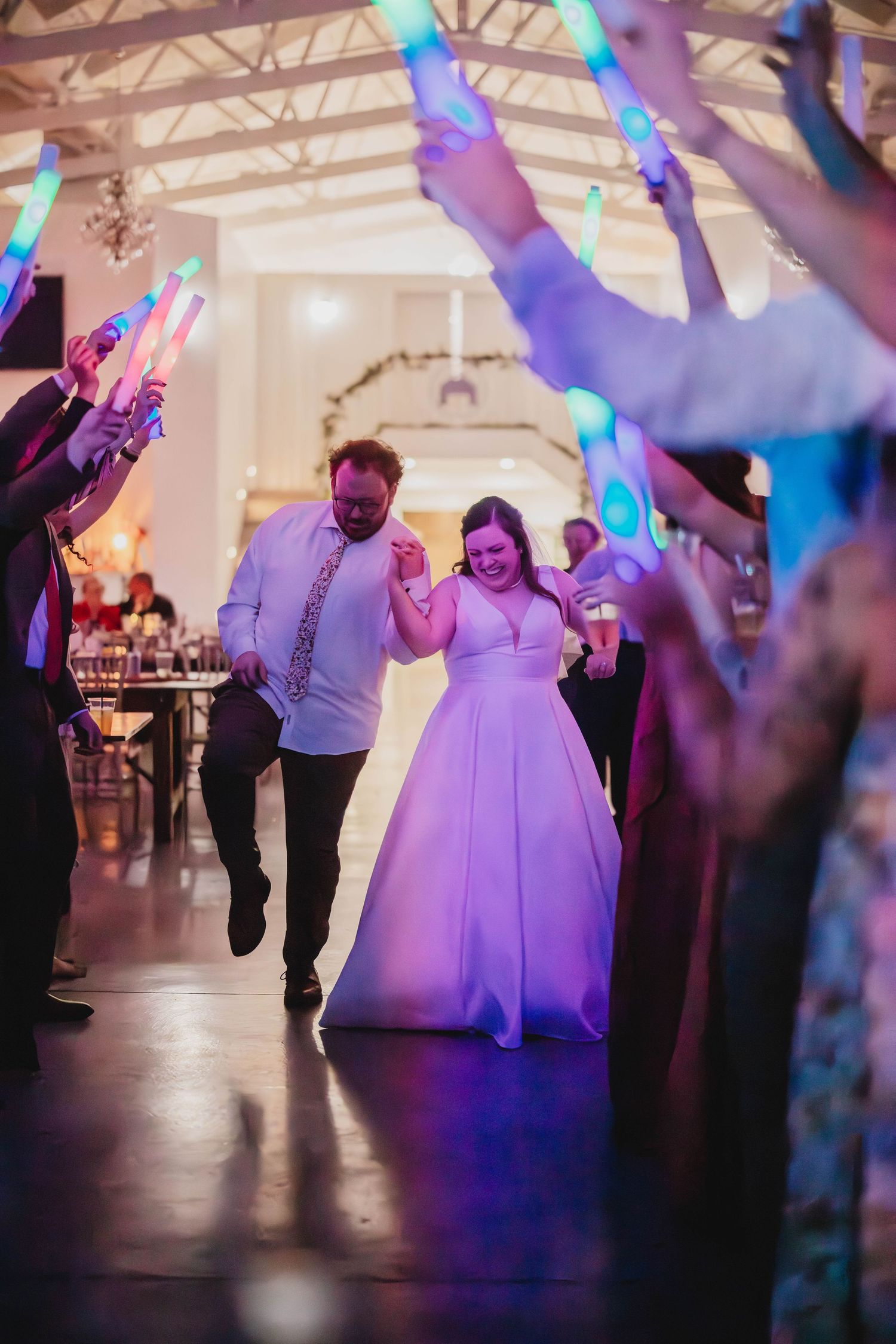 A couple in wedding attire dances under colorful glow sticks held up by wedding guests.