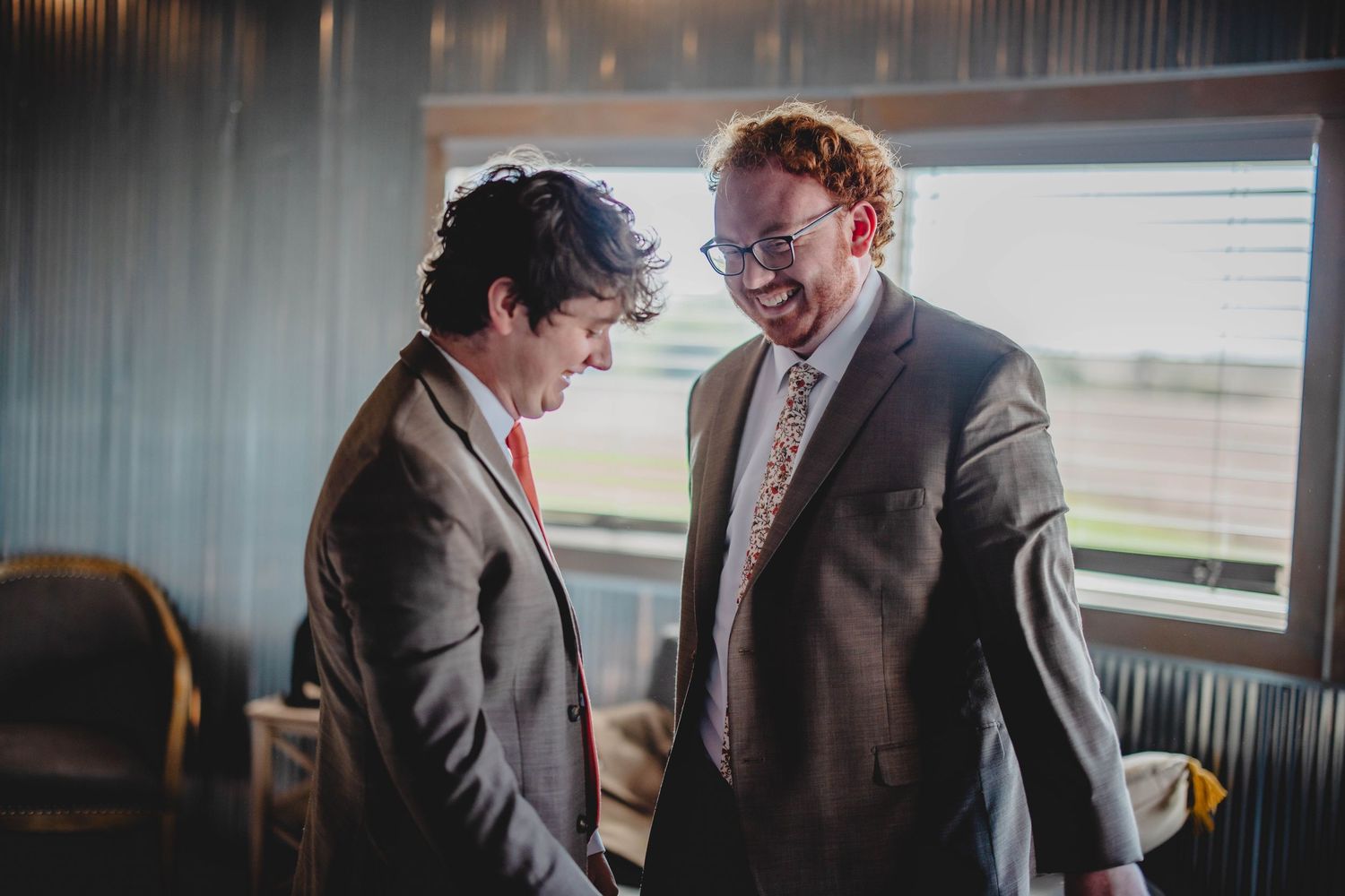 Two people in formal attire sharing a joyful moment by a window.