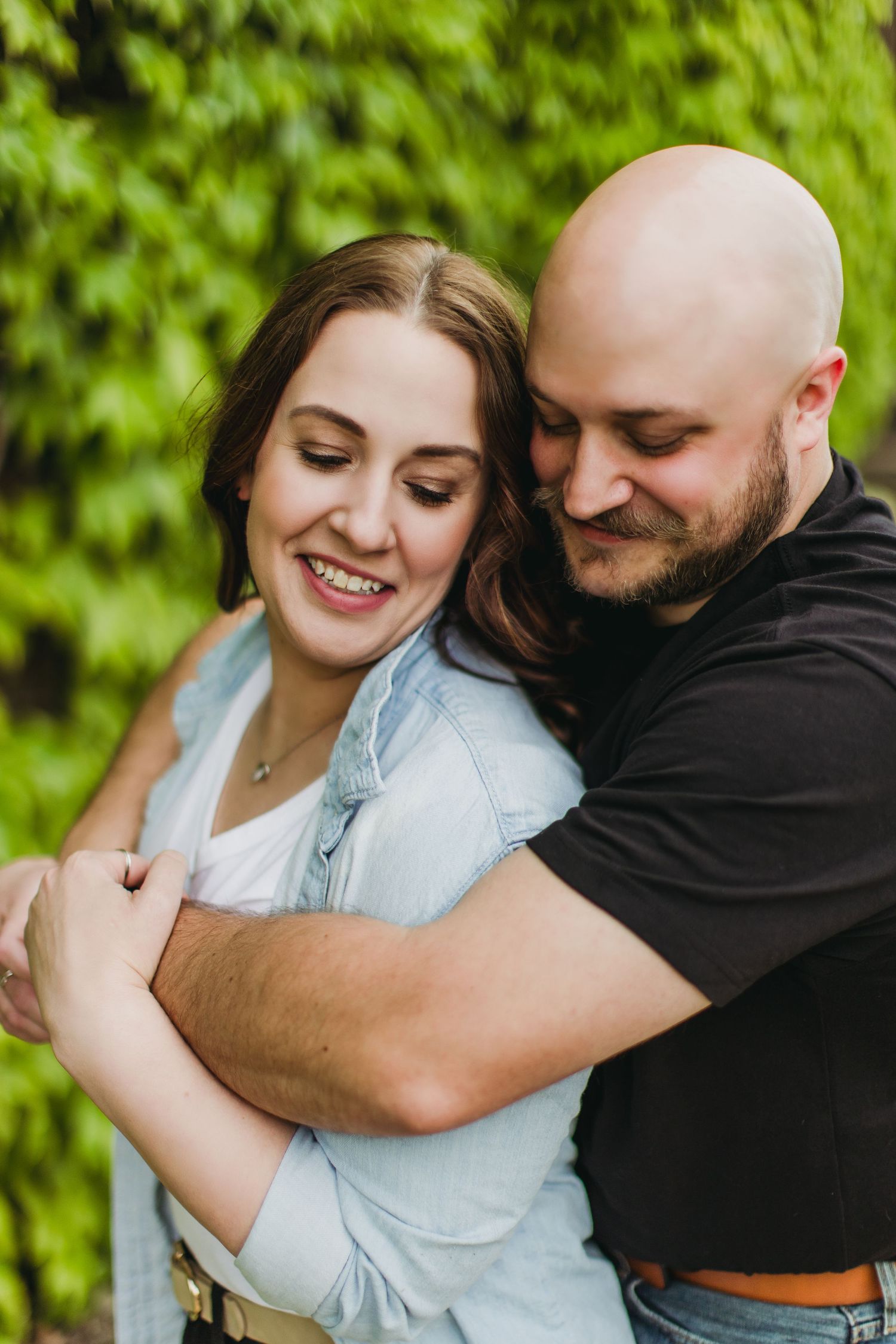 Intimate couple sharing a tender embrace and laughing together against green foliage.