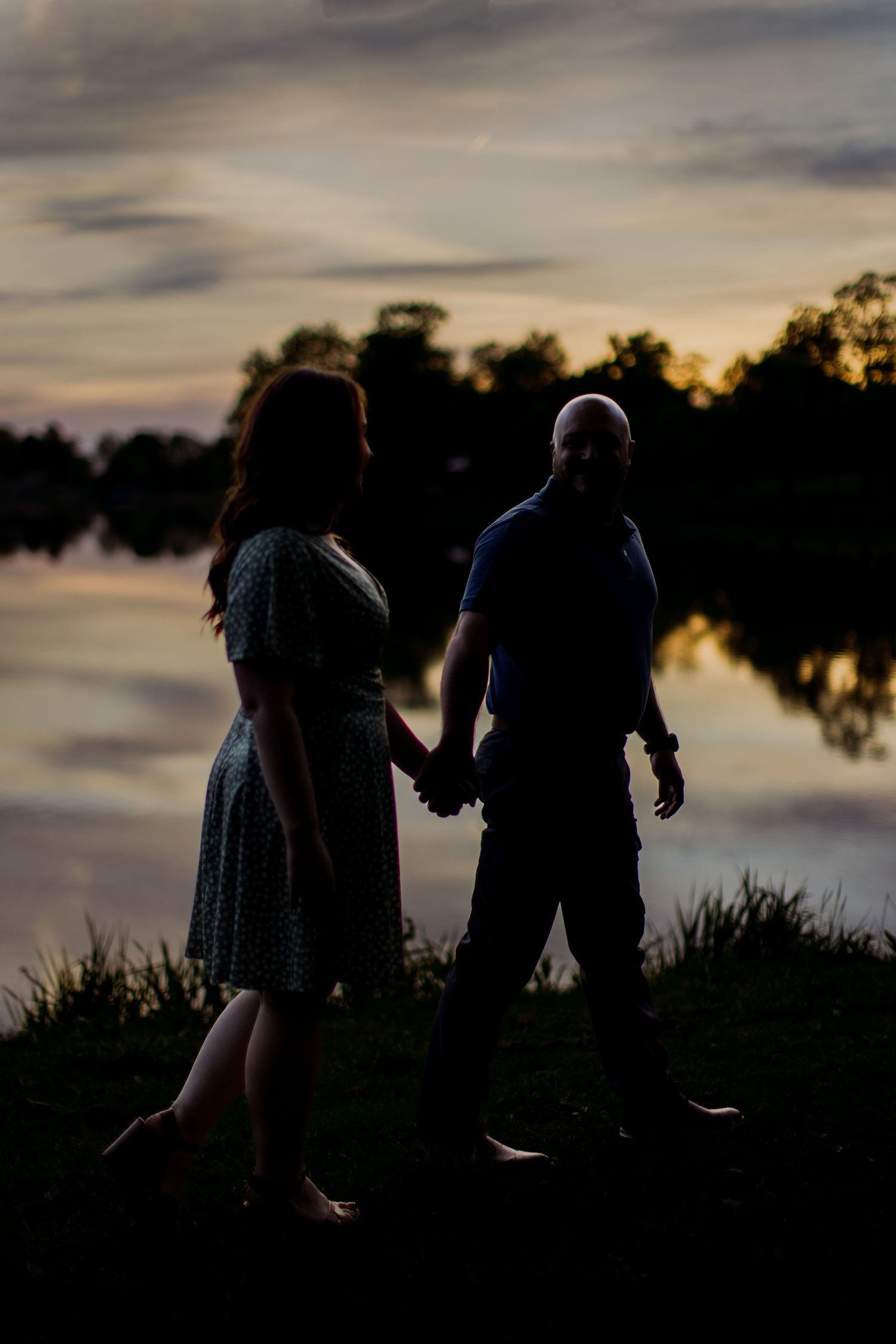 Two figures are silhouetted against a tranquil lake during golden hour.
