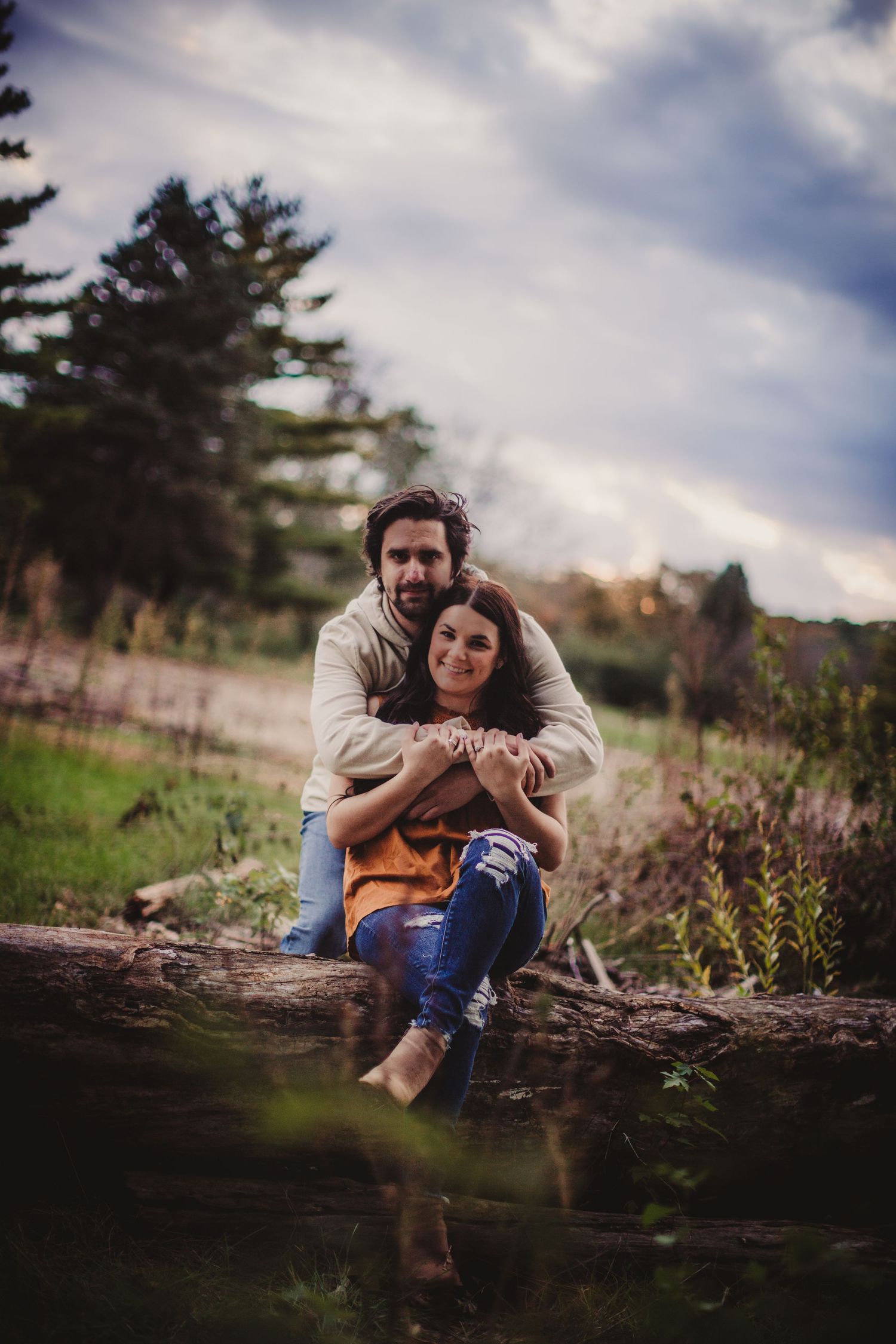Couple sitting on fallen log in nature setting during casual outdoor photoshoot.