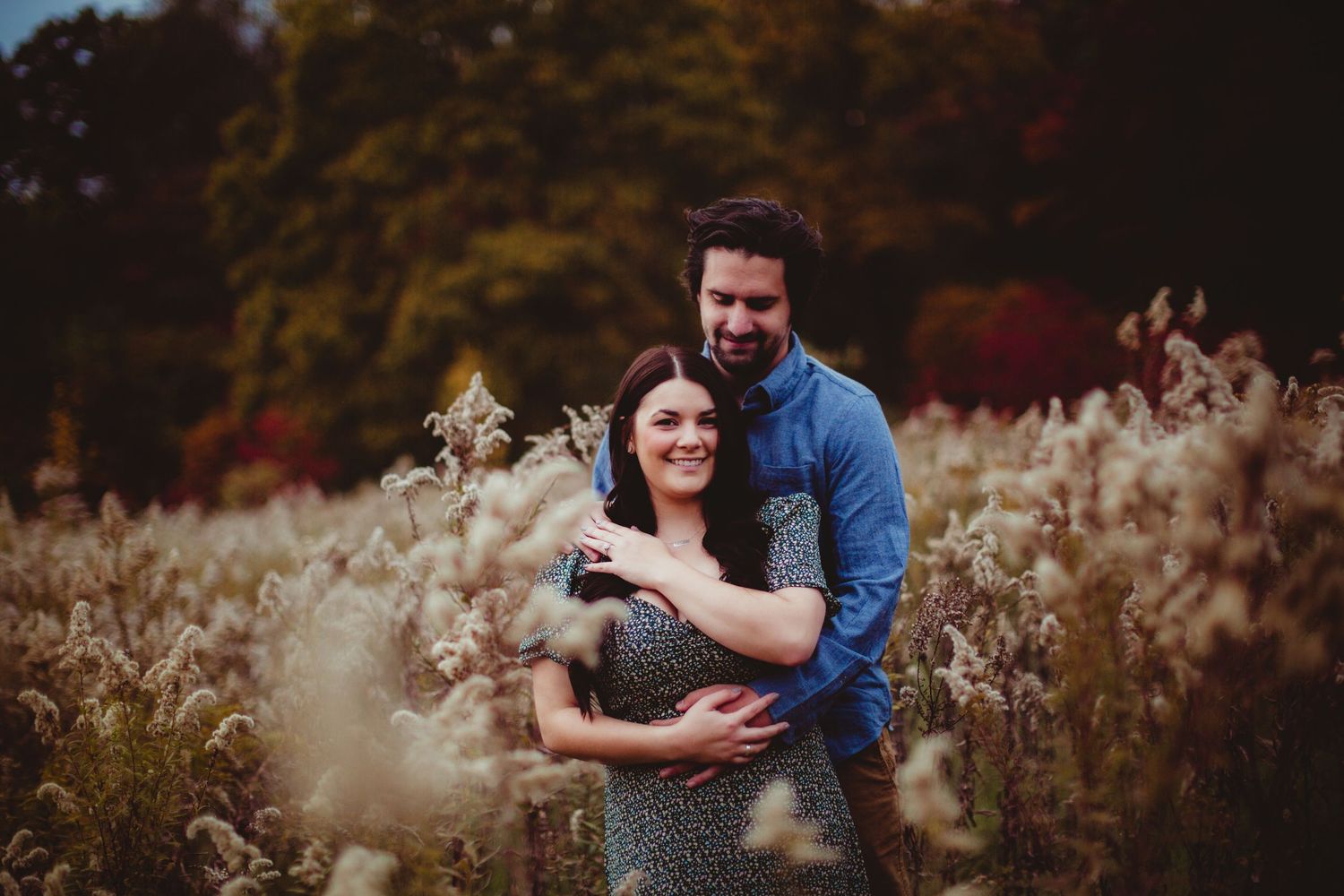 Couple shares romantic embrace surrounded by fall colors and wild grass.