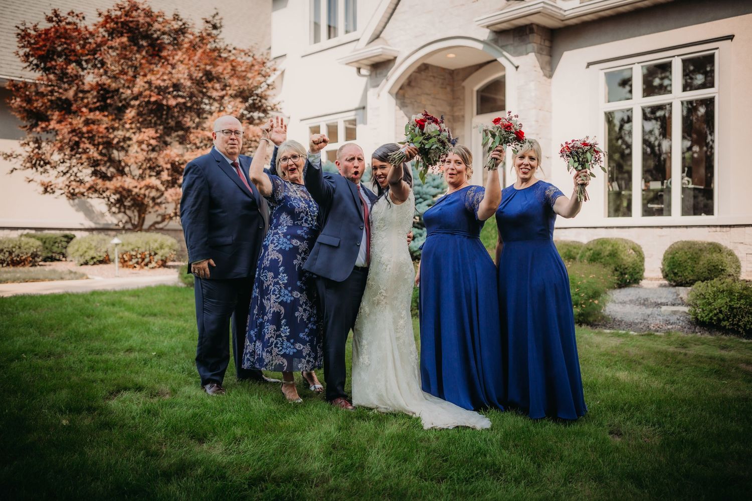 Wedding party gathers for formal photos outside a historic stone mansion.