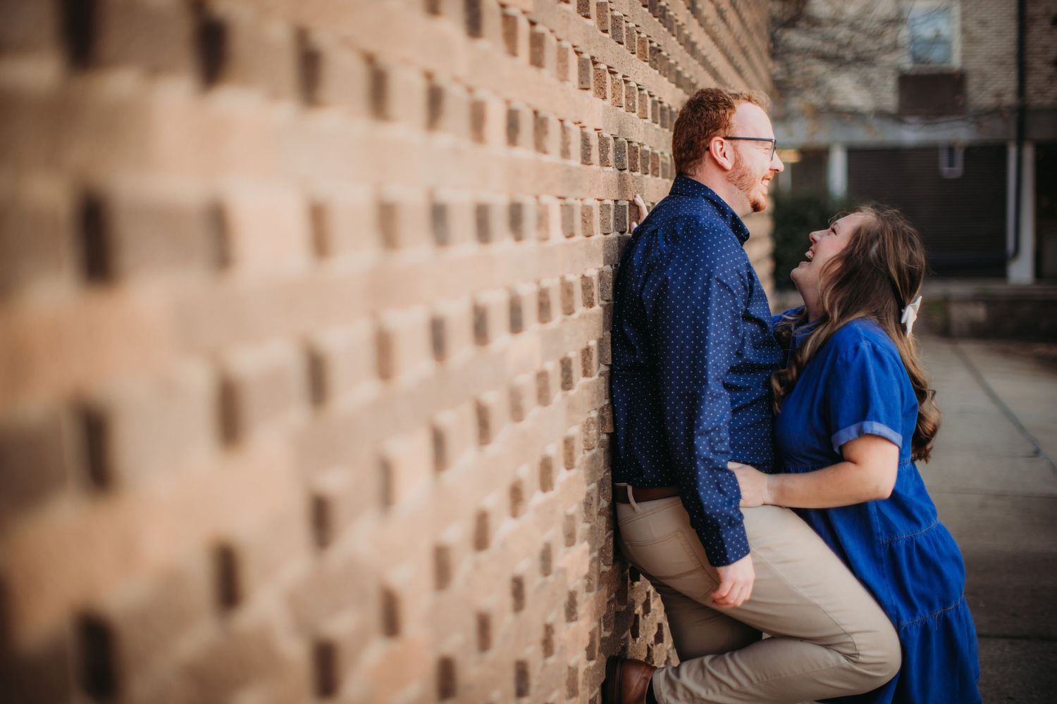 A tender embrace captured against an industrial brick wall with distinctive geometric patterns.
