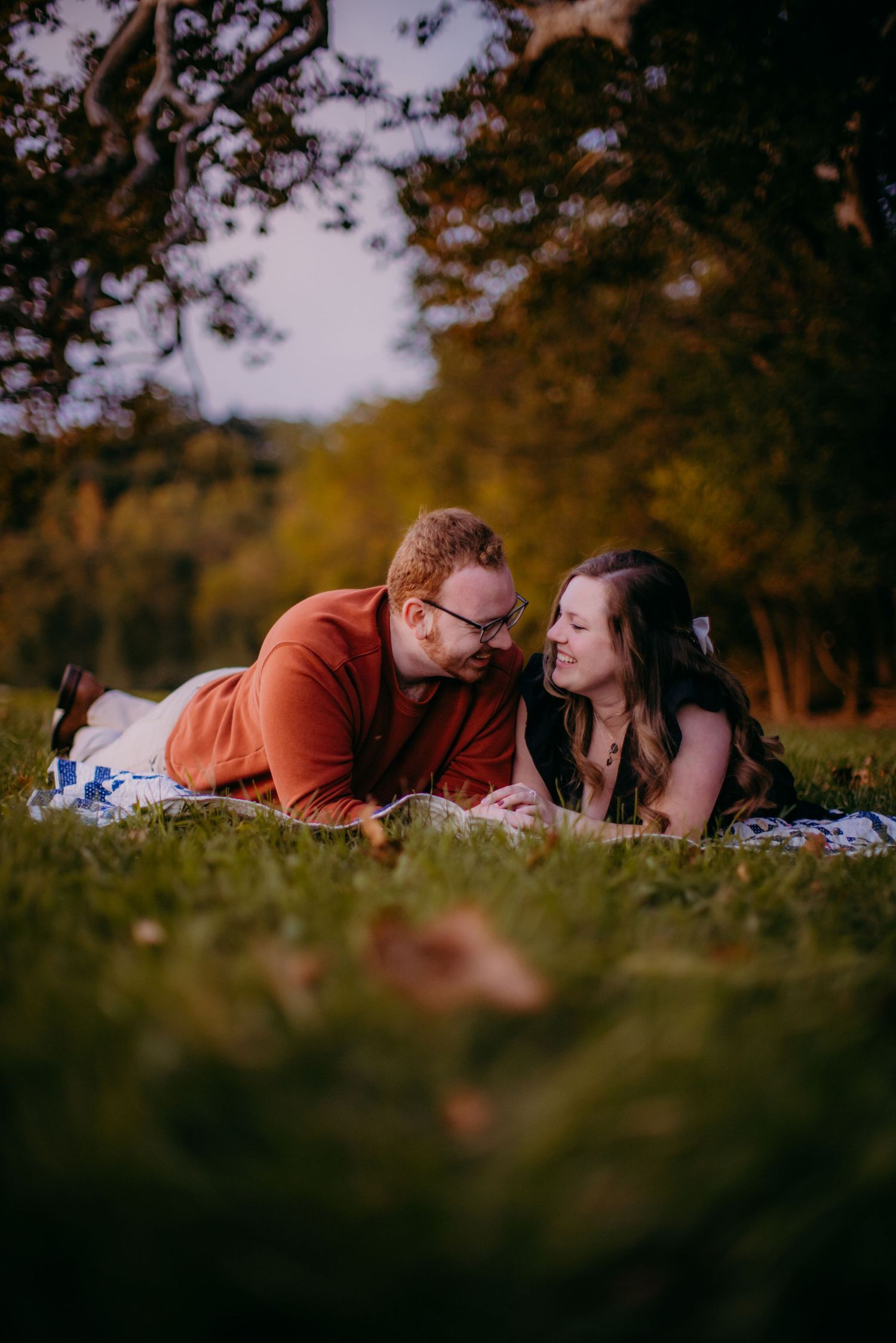 Couple lying on blue and white blanket having tender moment in fall foliage.
