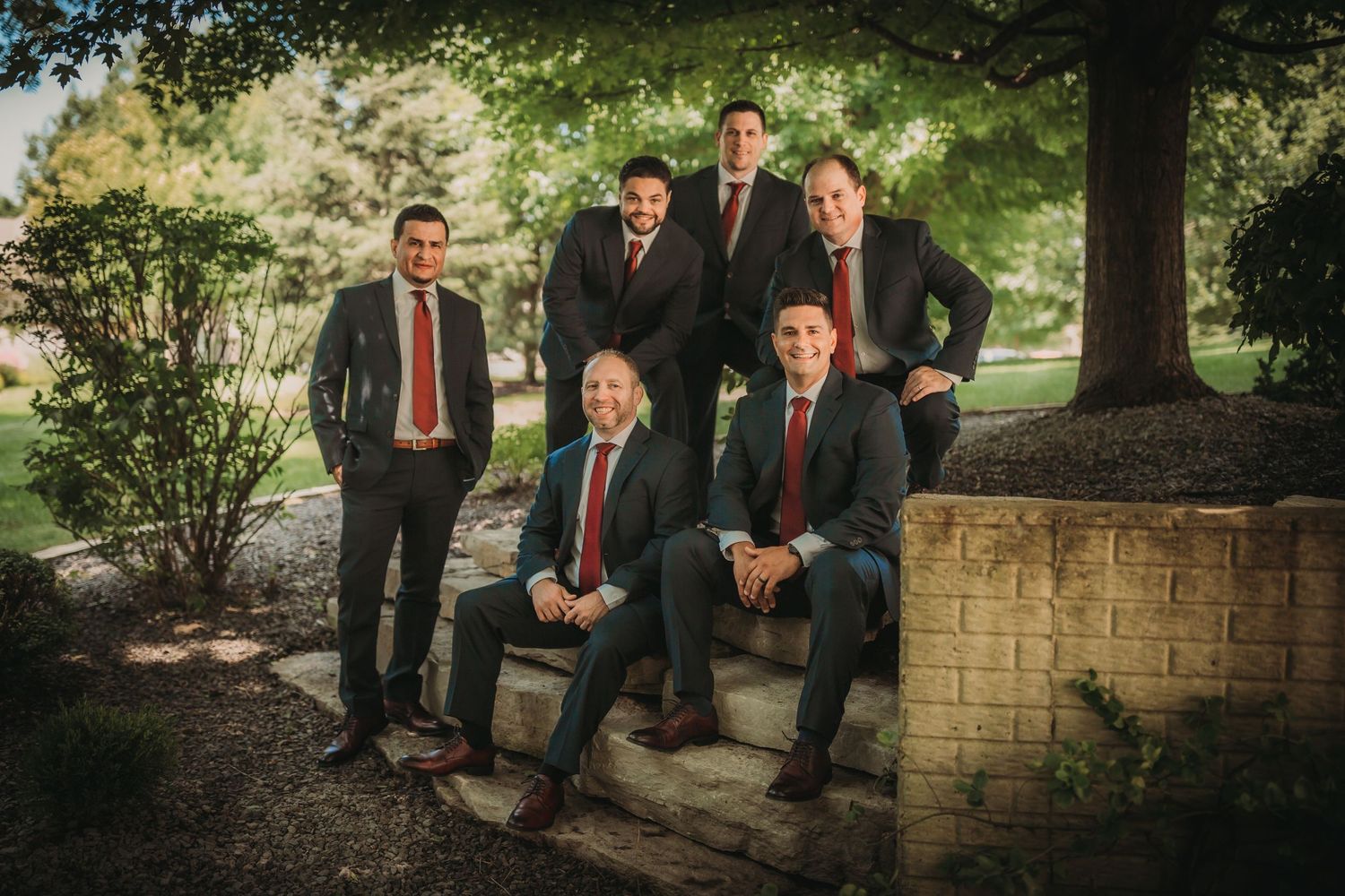 Modern groomsmen portrait on stone steps under trees in a natural outdoor setting.