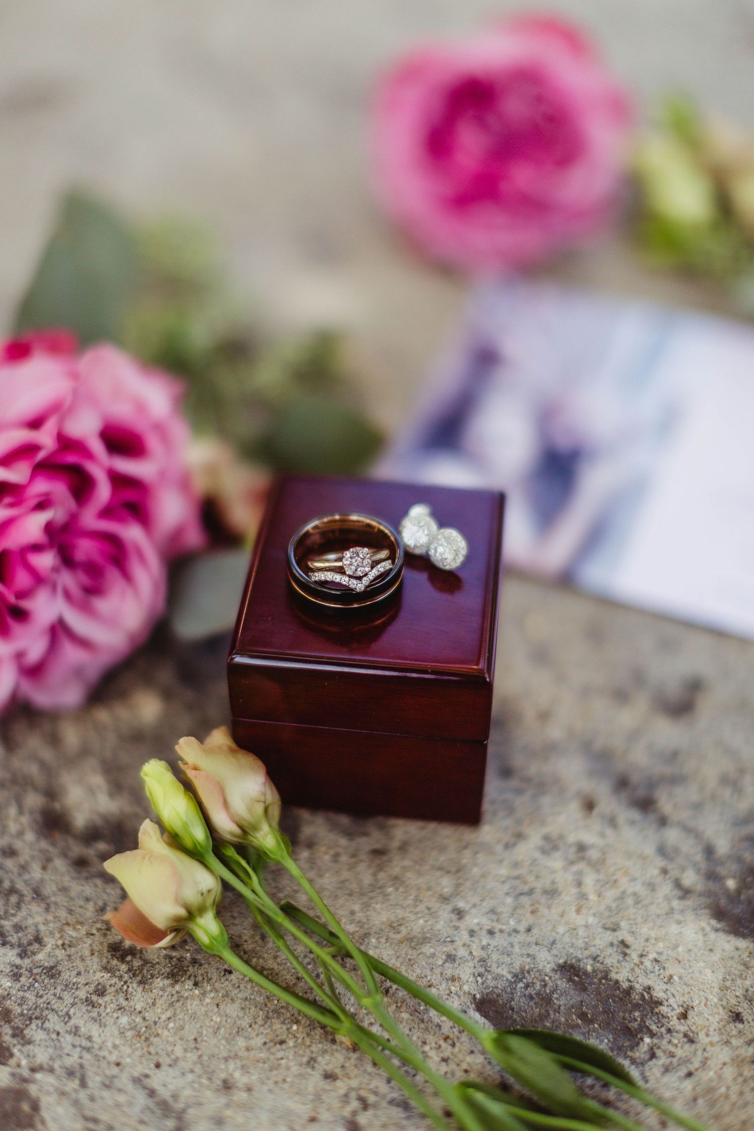 Wedding rings displayed on burgundy box with pink roses and greenery.