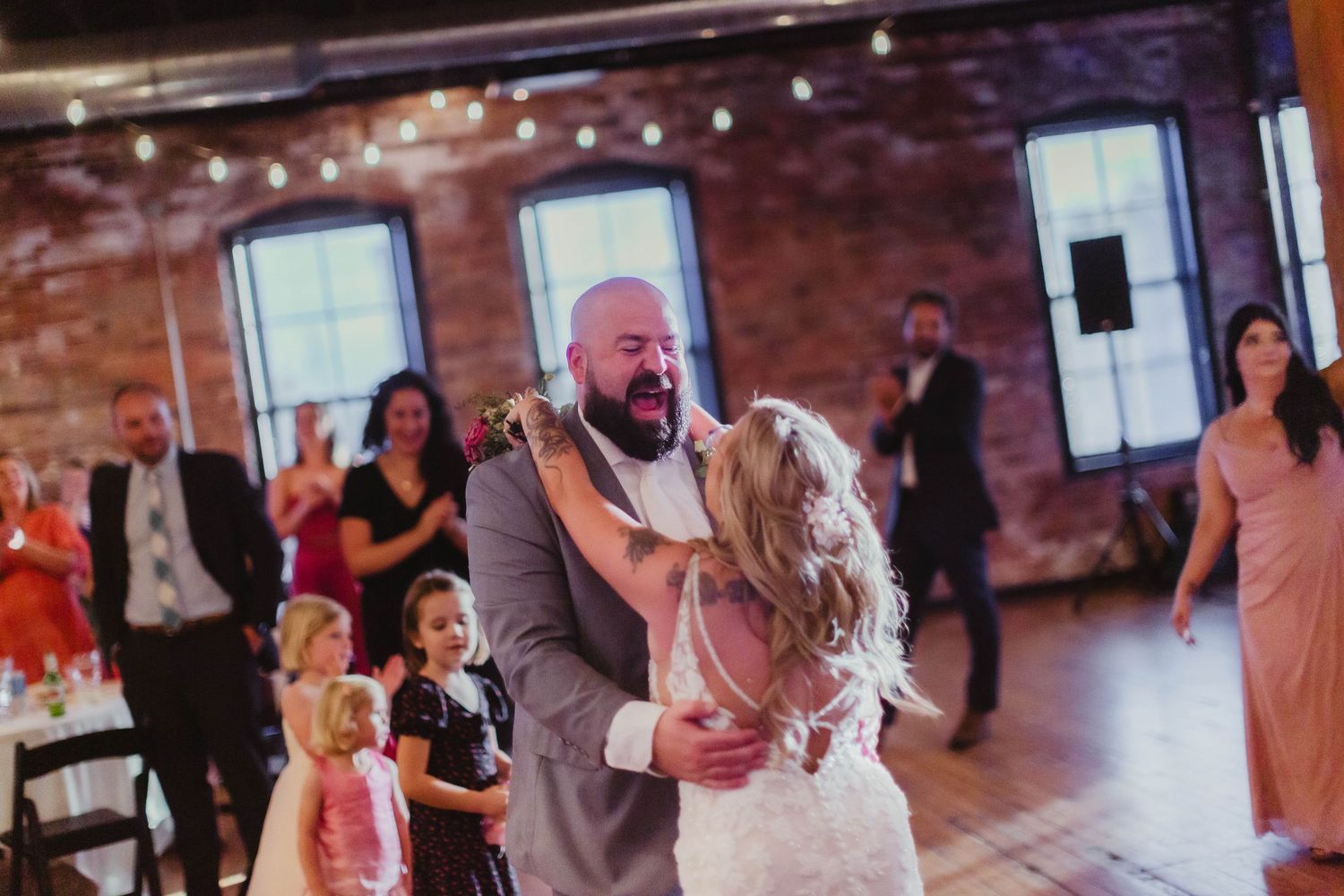 Newlyweds sharing their first dance at reception under warm string lights.