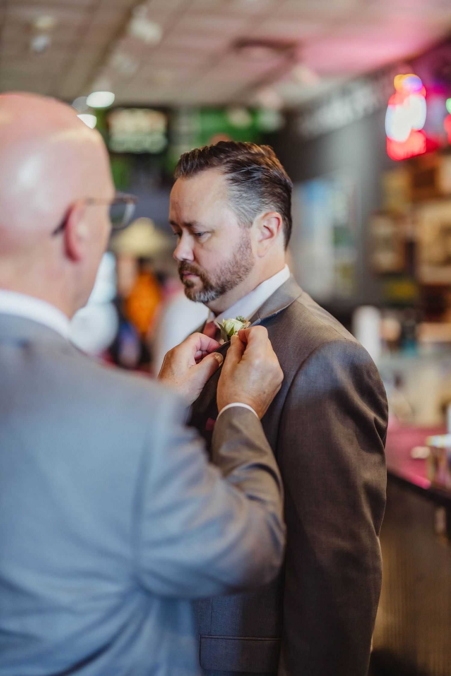 A bow tie is being adjusted on a person wearing a brown suit in a bar setting.